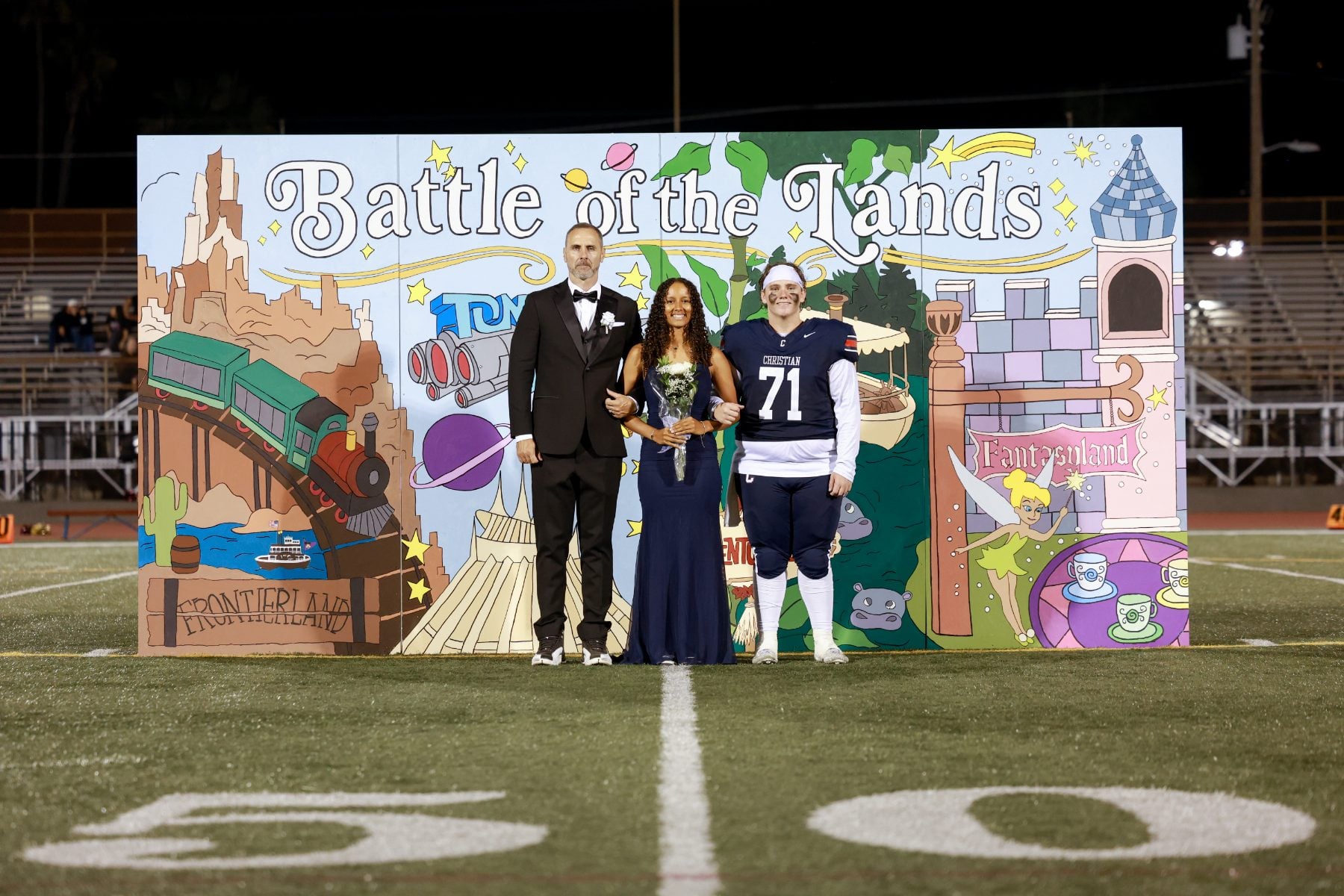 Homecoming court trio stands before Battle of the Lands backdrop, player #71