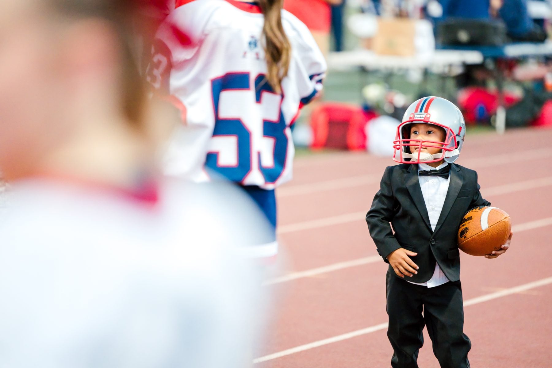 A boy in a tuxedo holds a football on the stadium track