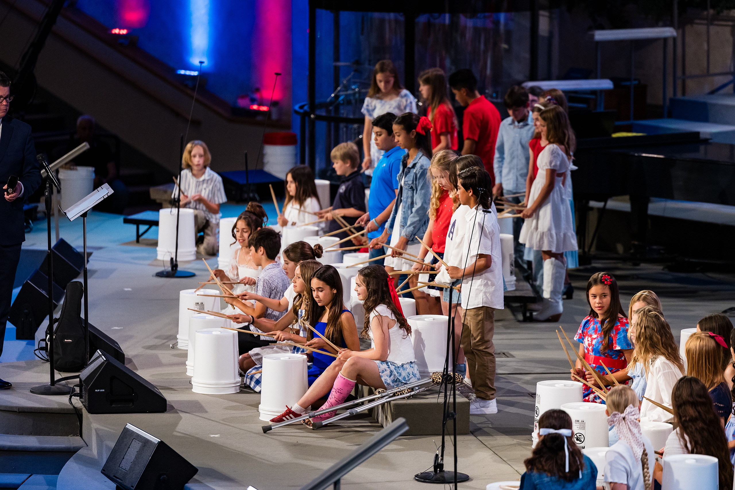 Christian Elementary East Celebrates Spring with “One Nation Under God” — 02 Students playing bucket drums with student narrator at microphone
