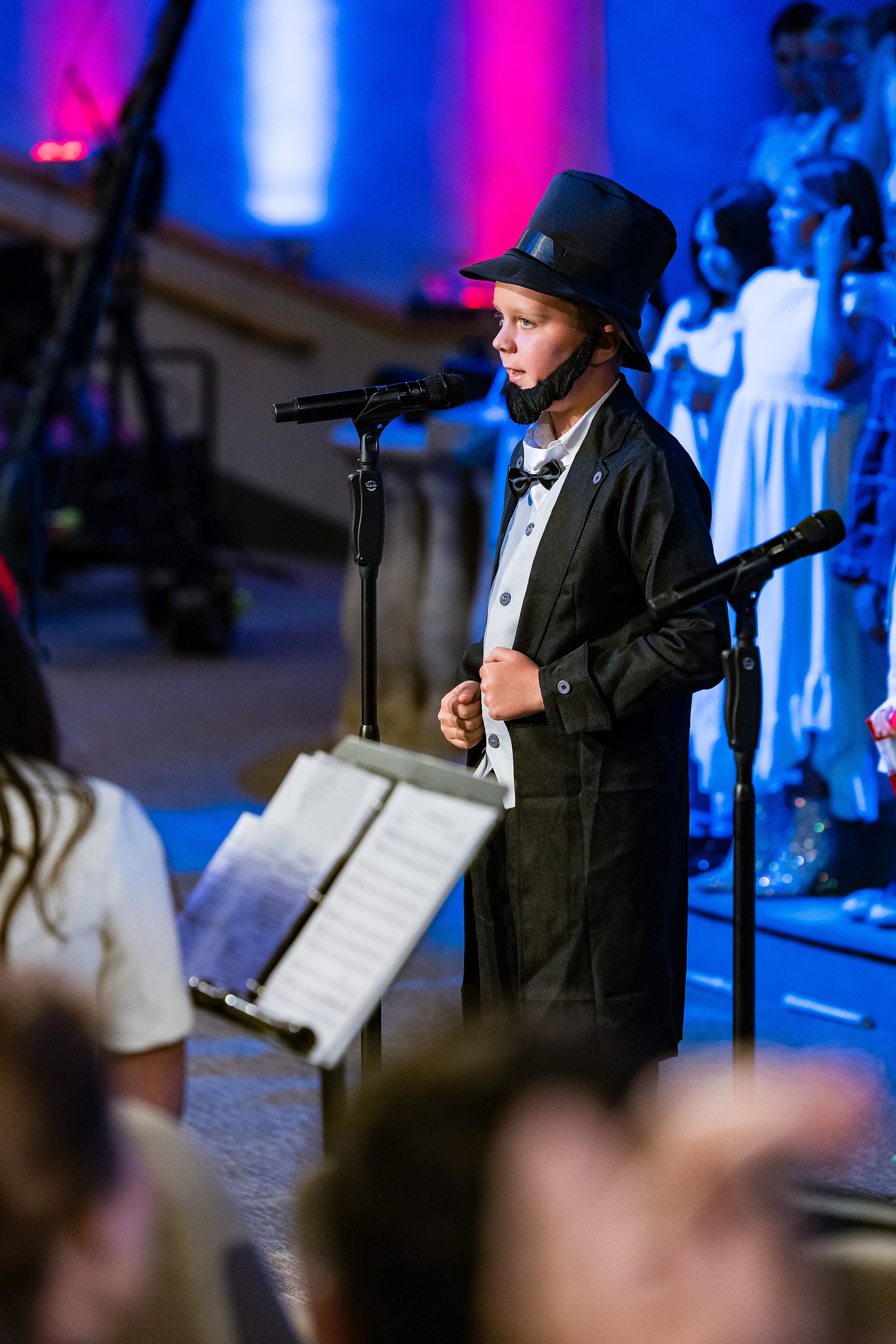Christian Elementary East Celebrates Spring with “One Nation Under God” — 07 Student in black coat and top hat playing historical character at microphone