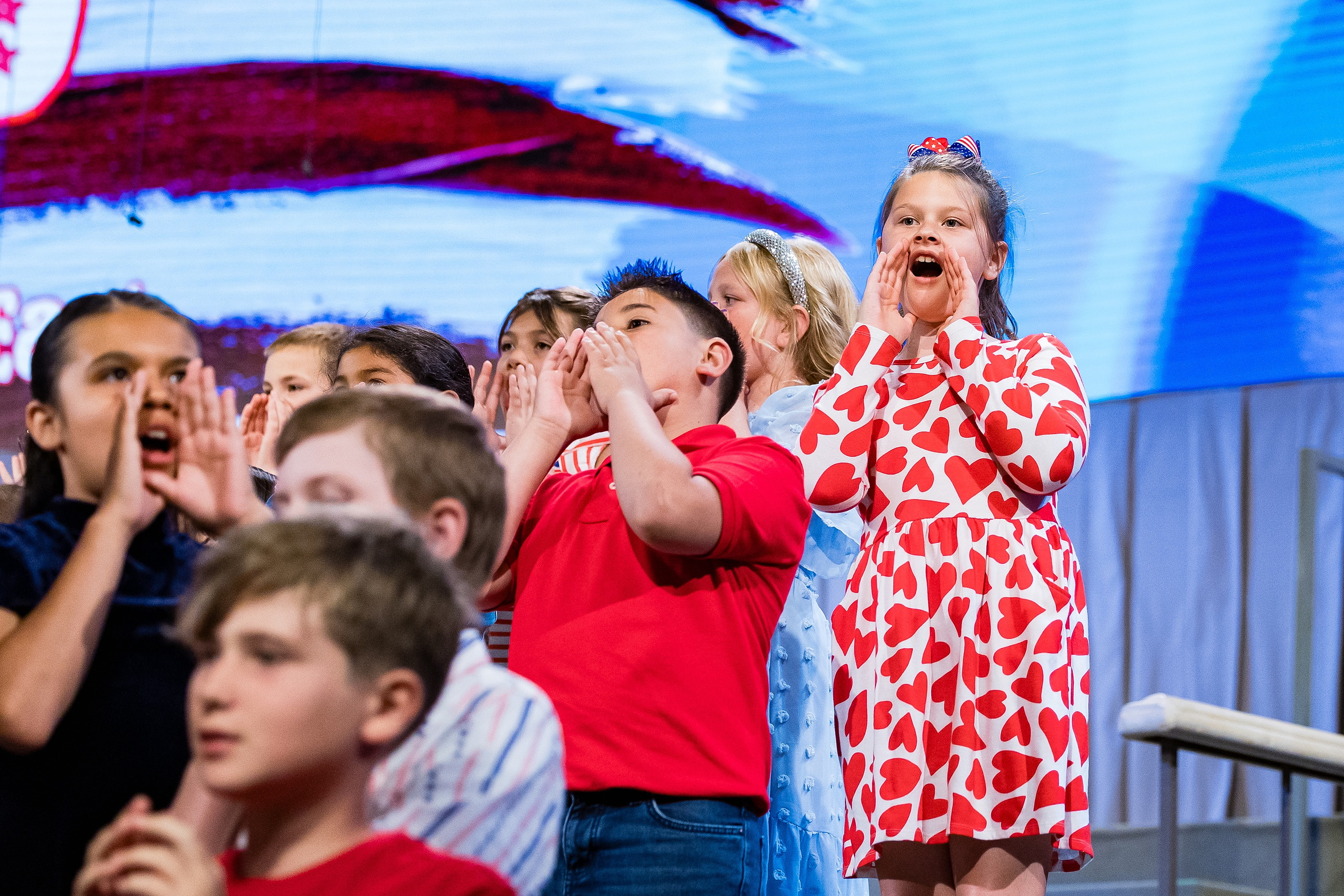 Christian Elementary East Celebrates Spring with “One Nation Under God” — 10 Younger elementary students singing with animated joyful expressions