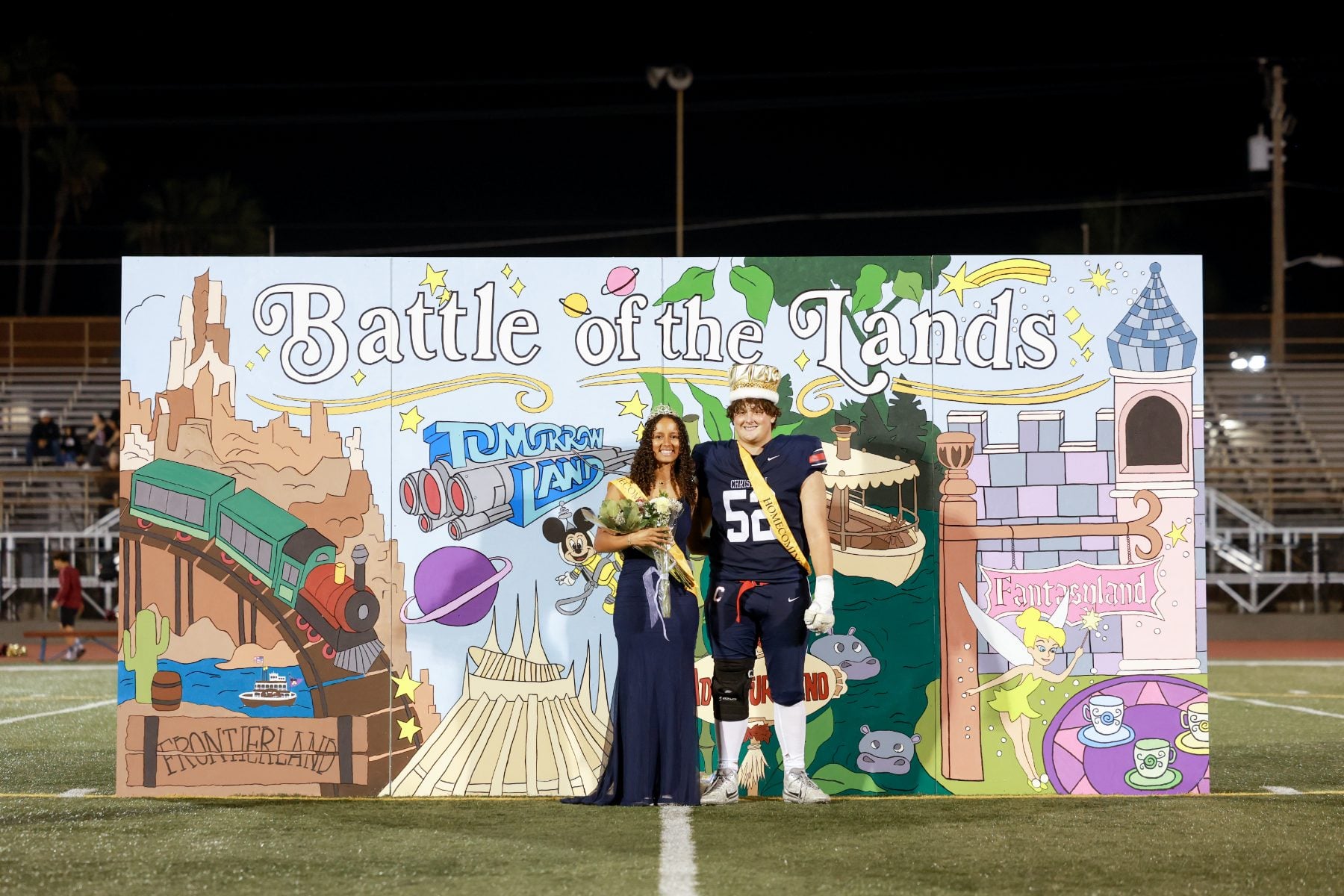 Homecoming queen and football player pose at the Battle of the Lands backdrop