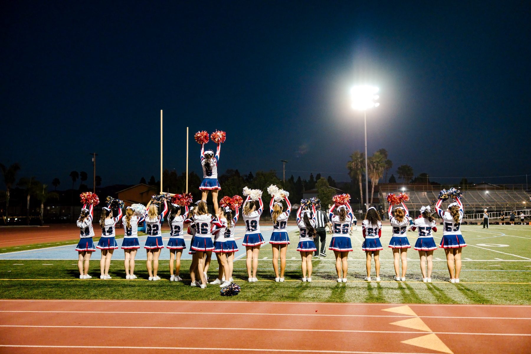Cheerleaders perform a stunt on the football field under stadium lights