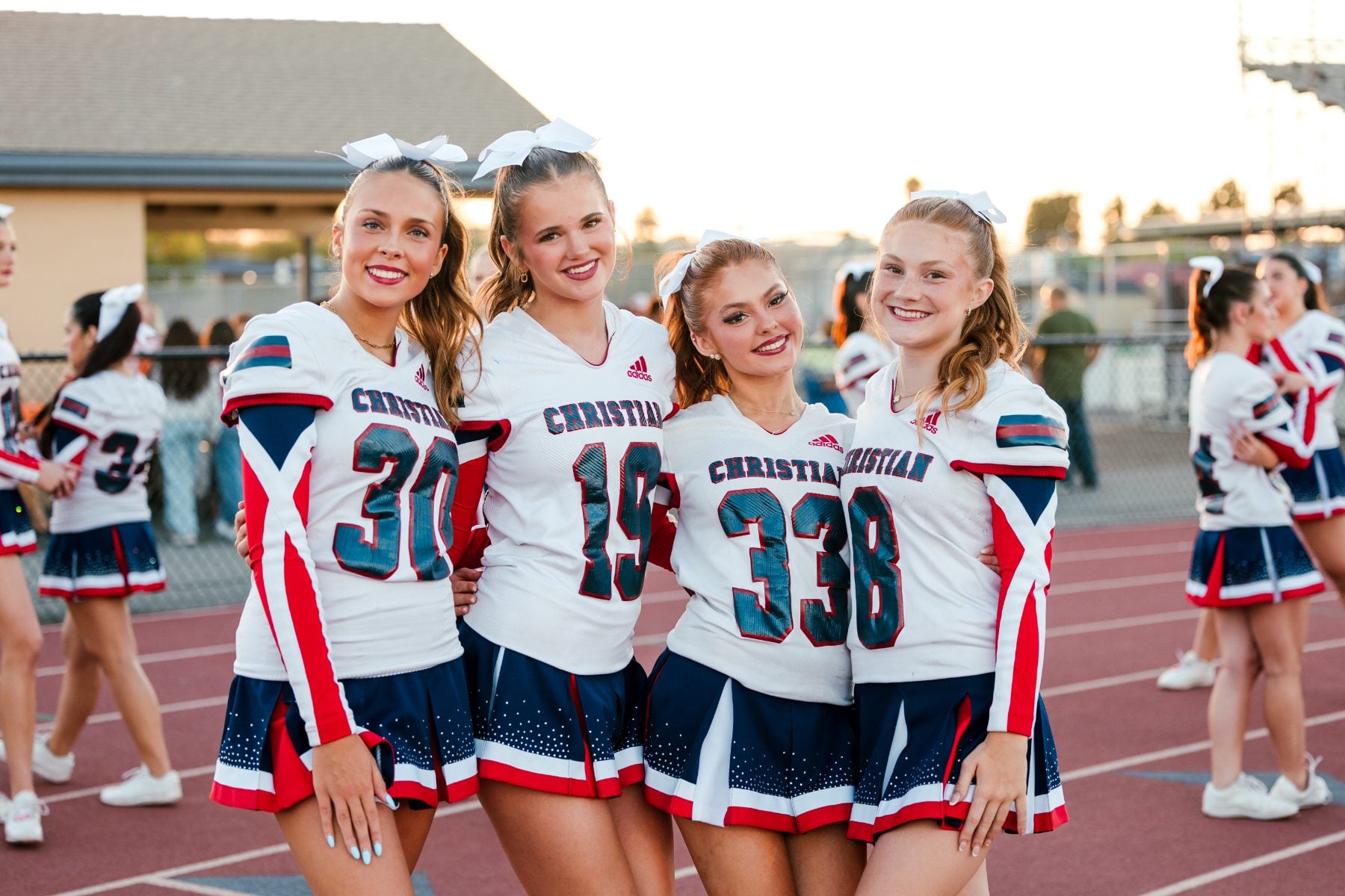 Four cheerleaders in Patriots uniforms smile together on the track