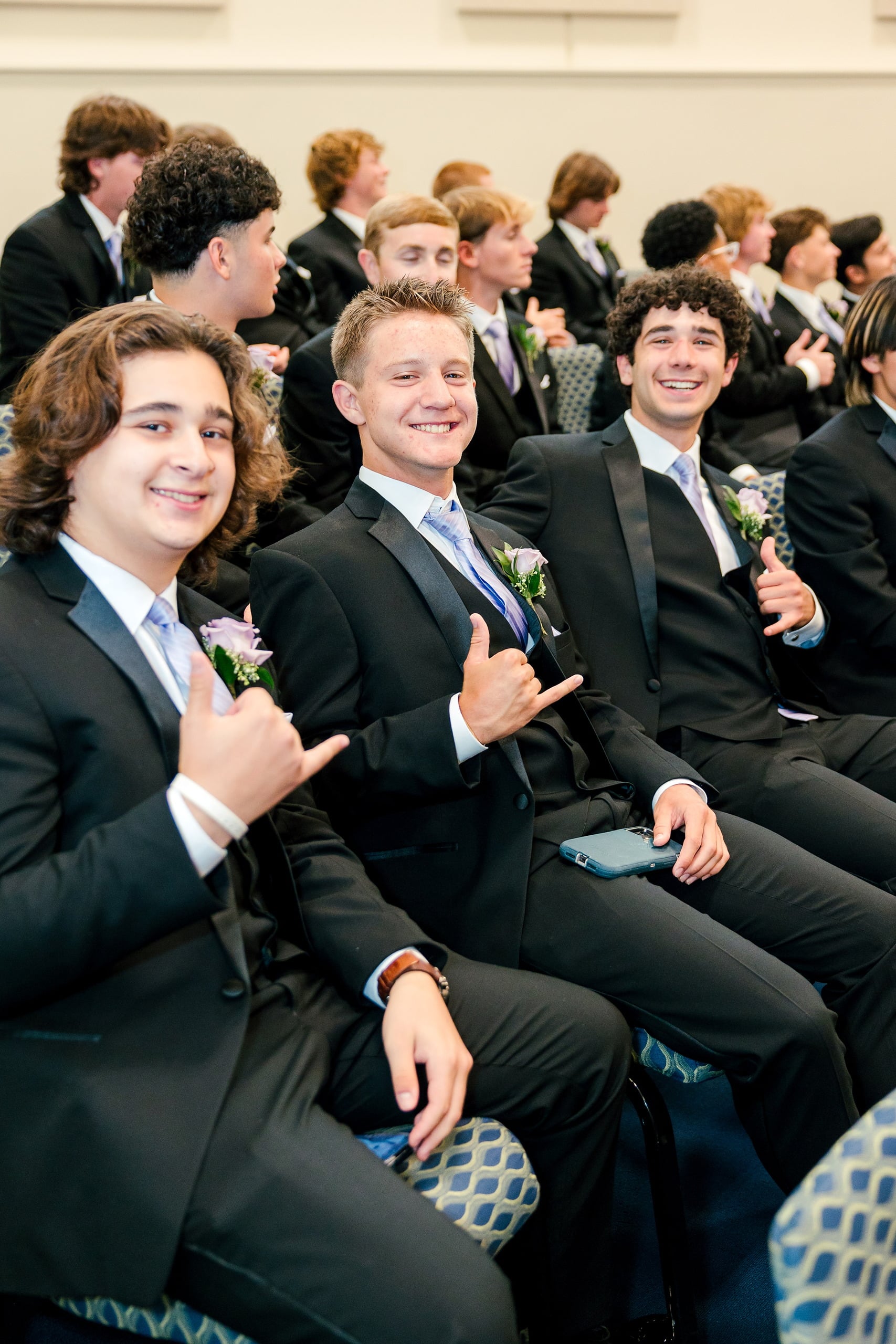 Christian High School Commencement 2025: Rise Up — 07 Three male graduates in black suits sit together giving thumbs up and grinning