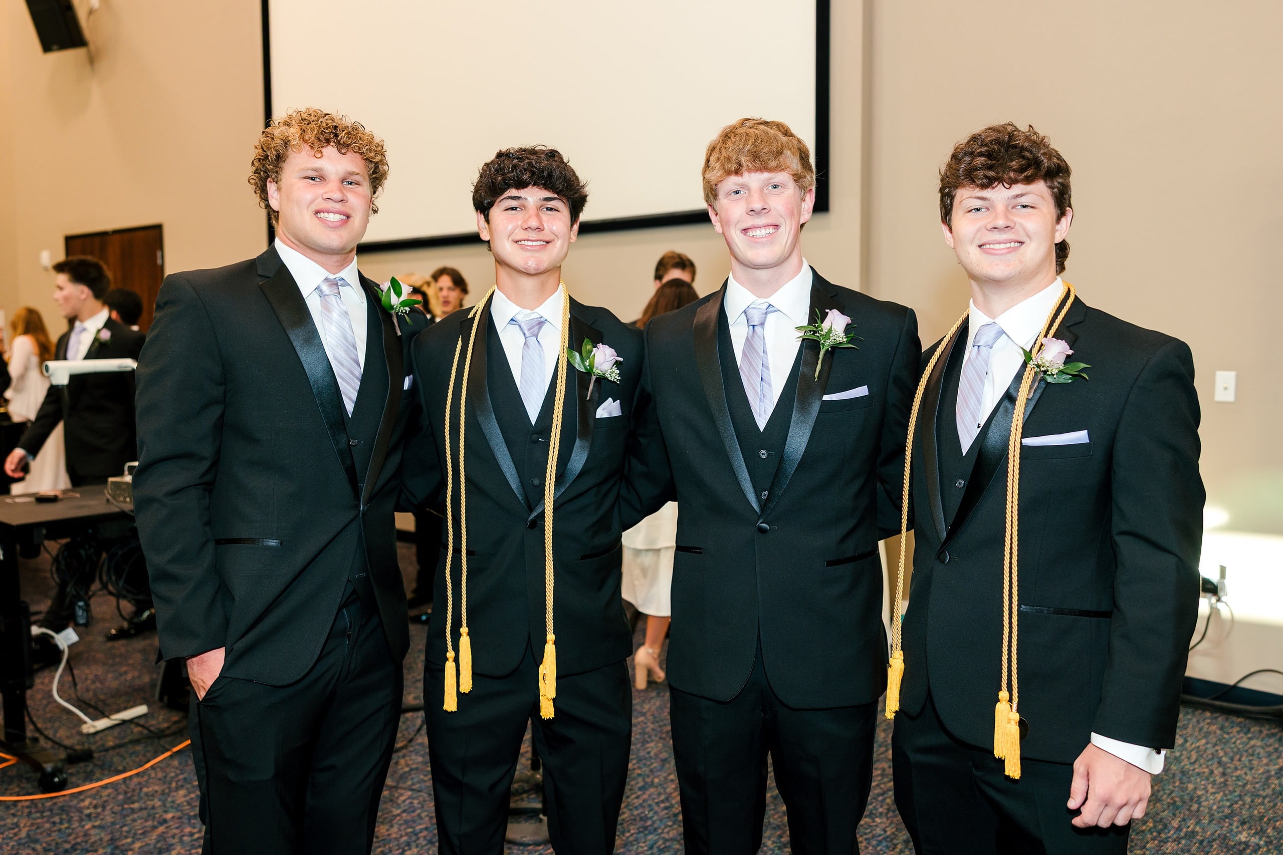 Christian High School Commencement 2025: Rise Up — 10 Four male graduates in black suits and gold cords stand together at the ceremony
