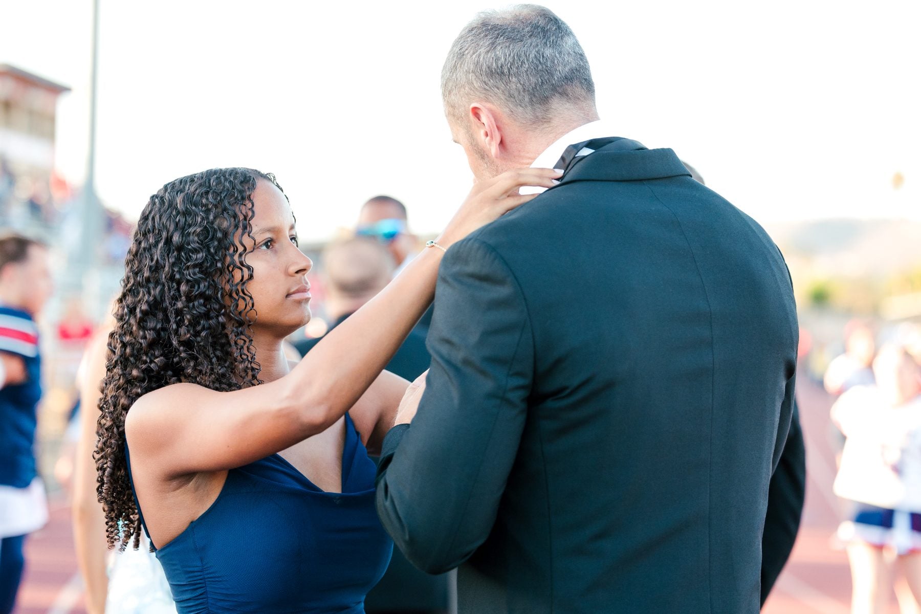 Woman adjusts a man's jacket collar on the football field at dusk