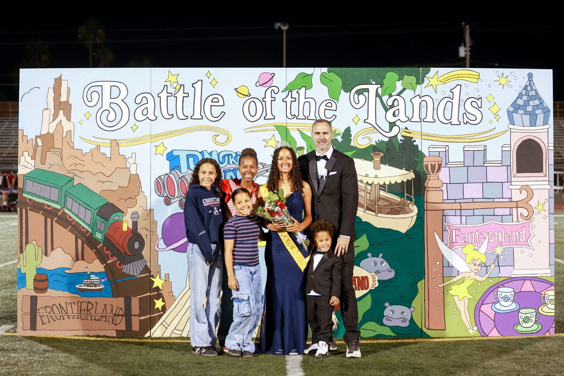 Homecoming court family poses before Battle of the Lands backdrop at Christian High School
