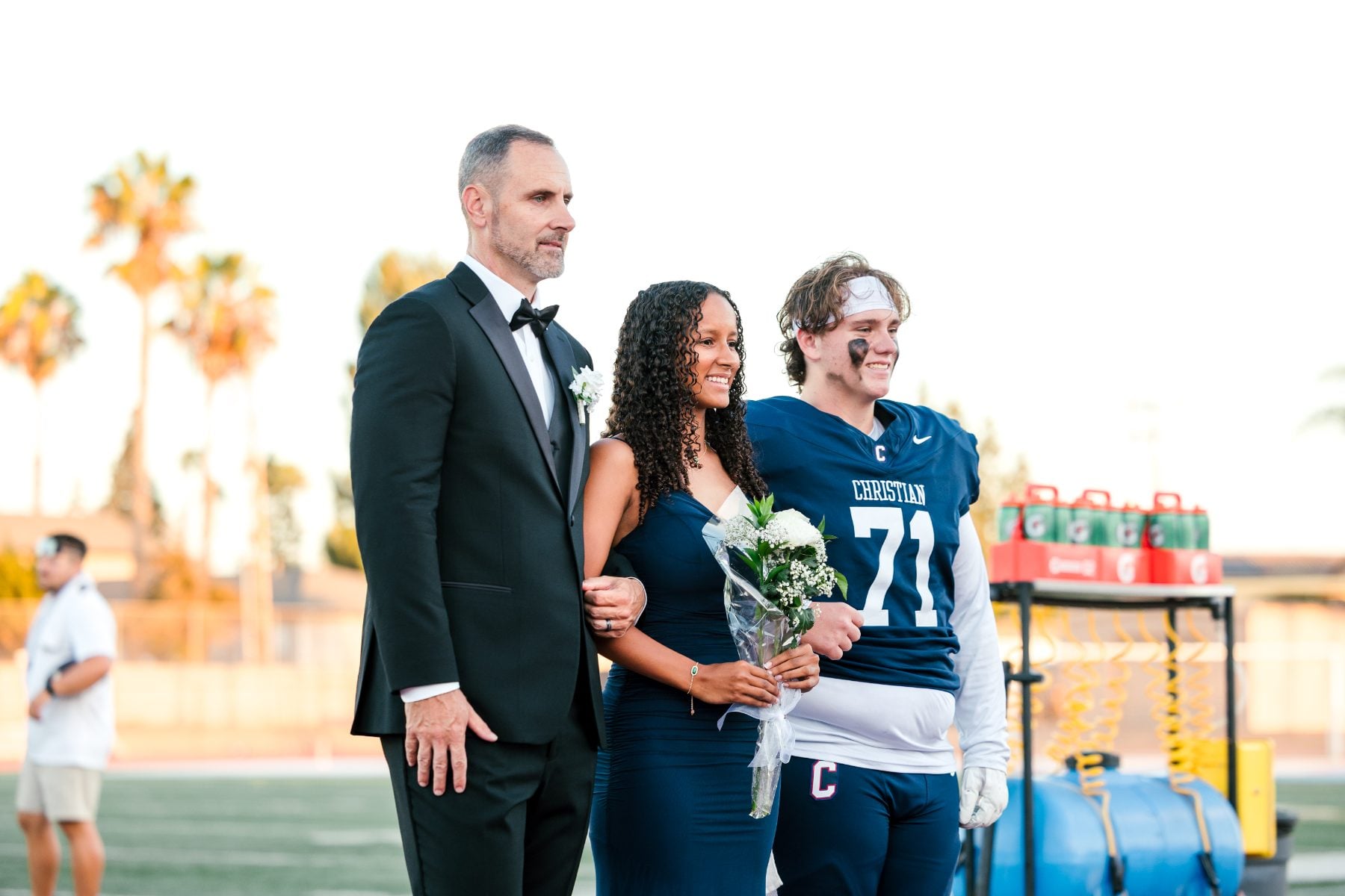 Homecoming court student holds bouquet beside father and Patriots football player