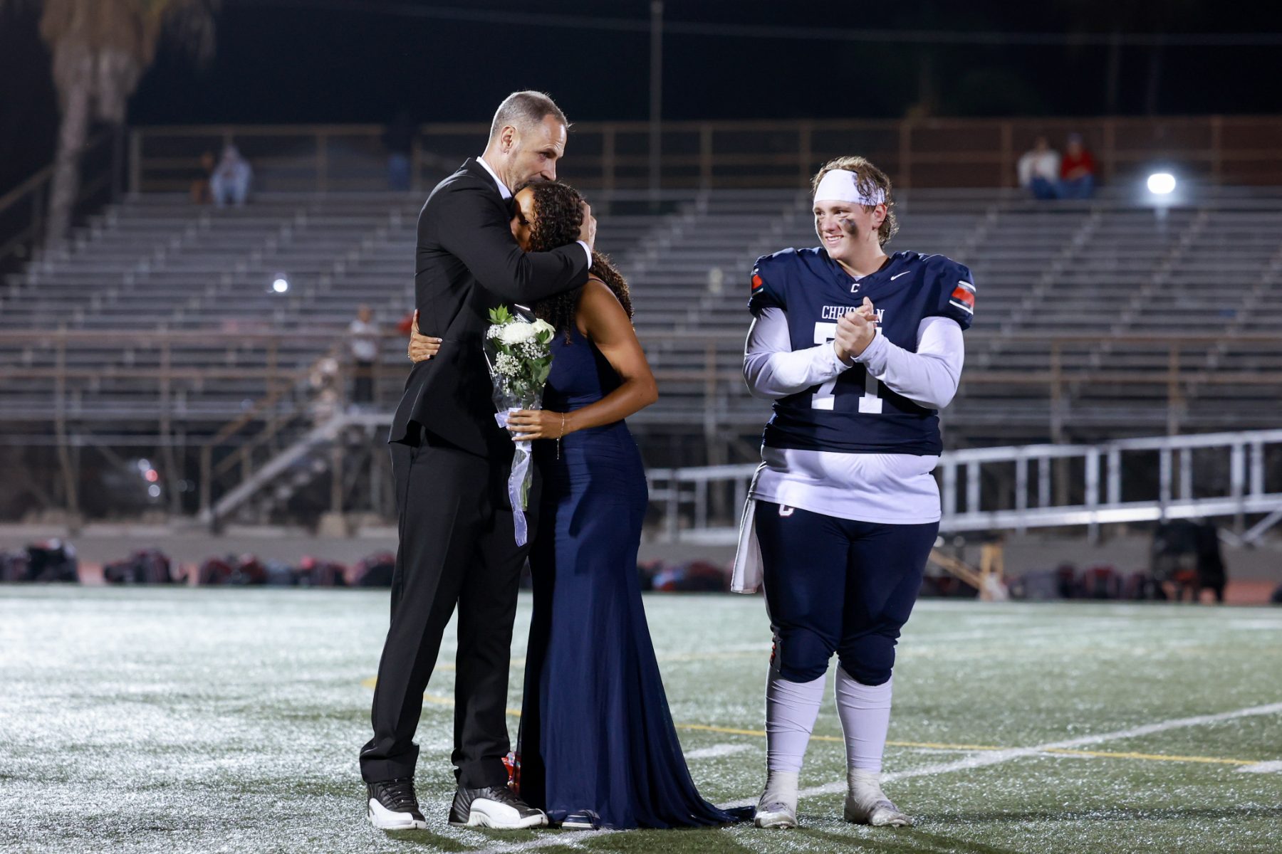 A man and woman embrace on the field as a Patriots player claps nearby