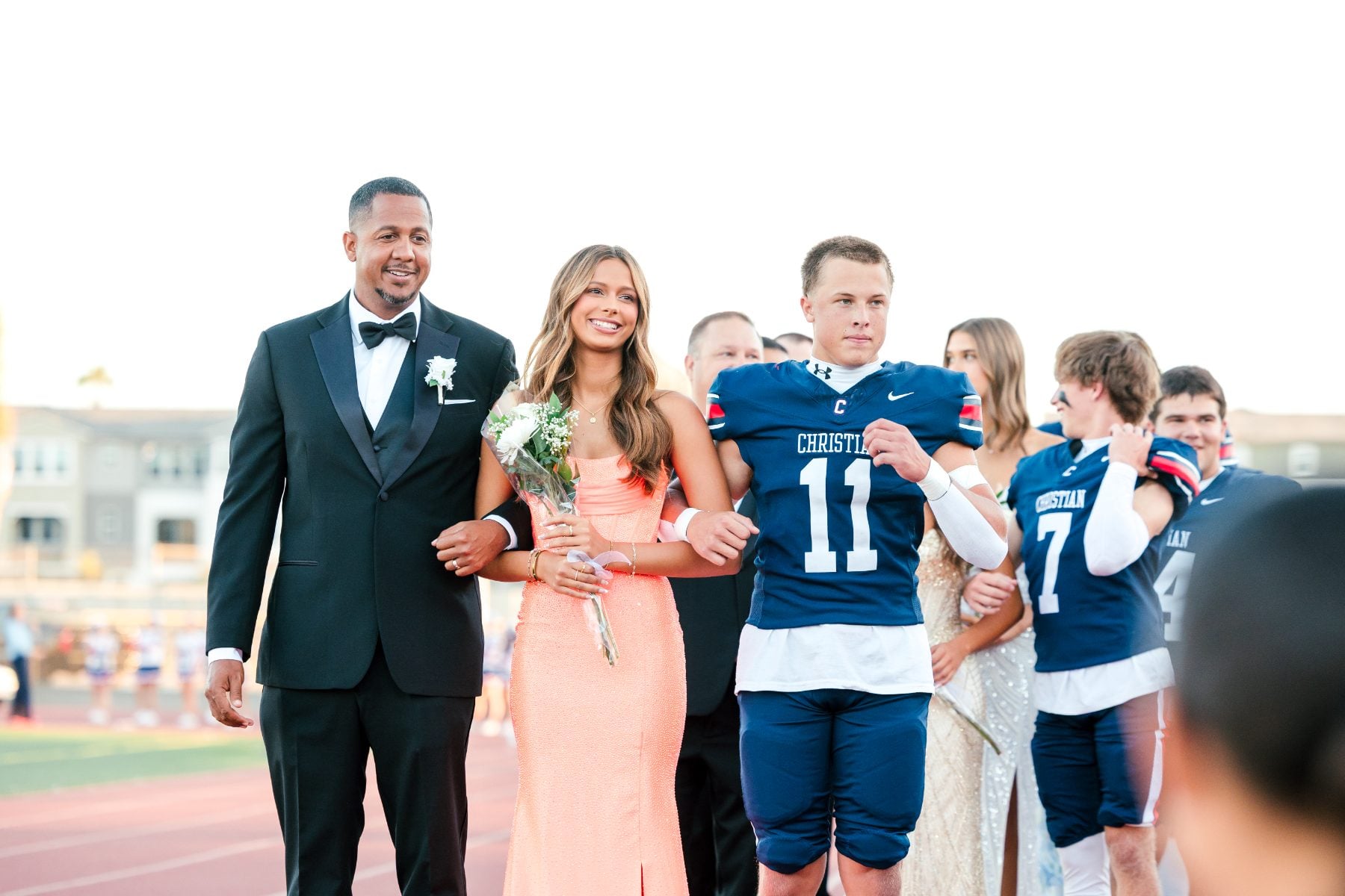 Homecoming court escorts walk the field with a Christian High School football player