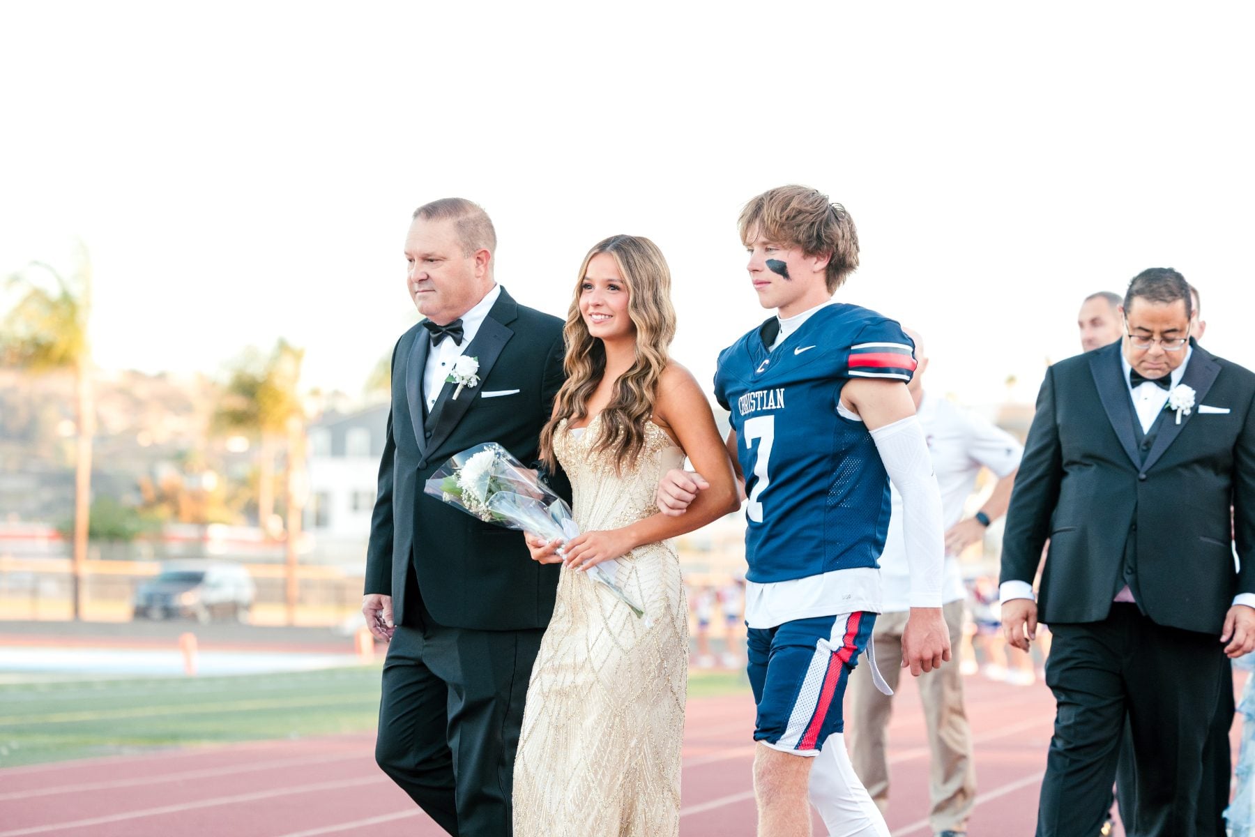 Homecoming court escorts a Christian High School football player across the track