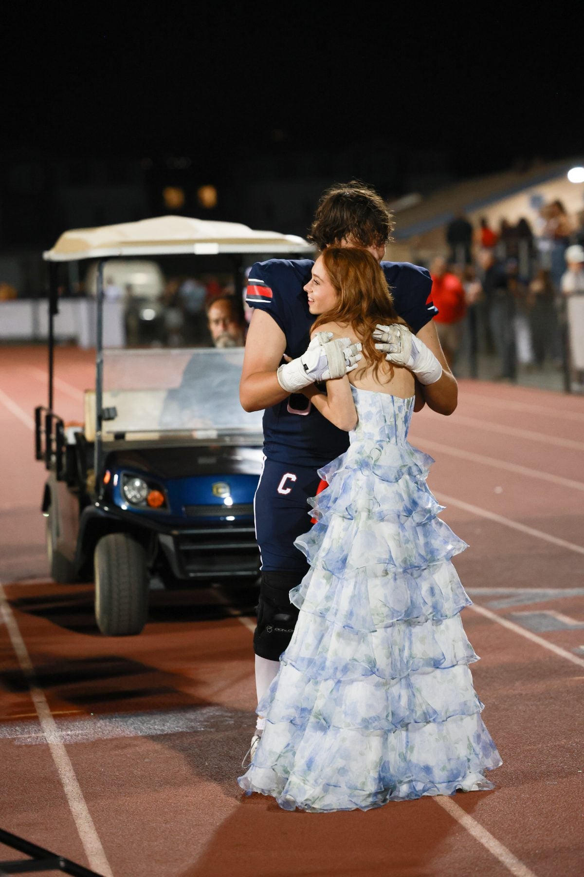 Football player in jersey number 7 embraces date in blue gown near a cart