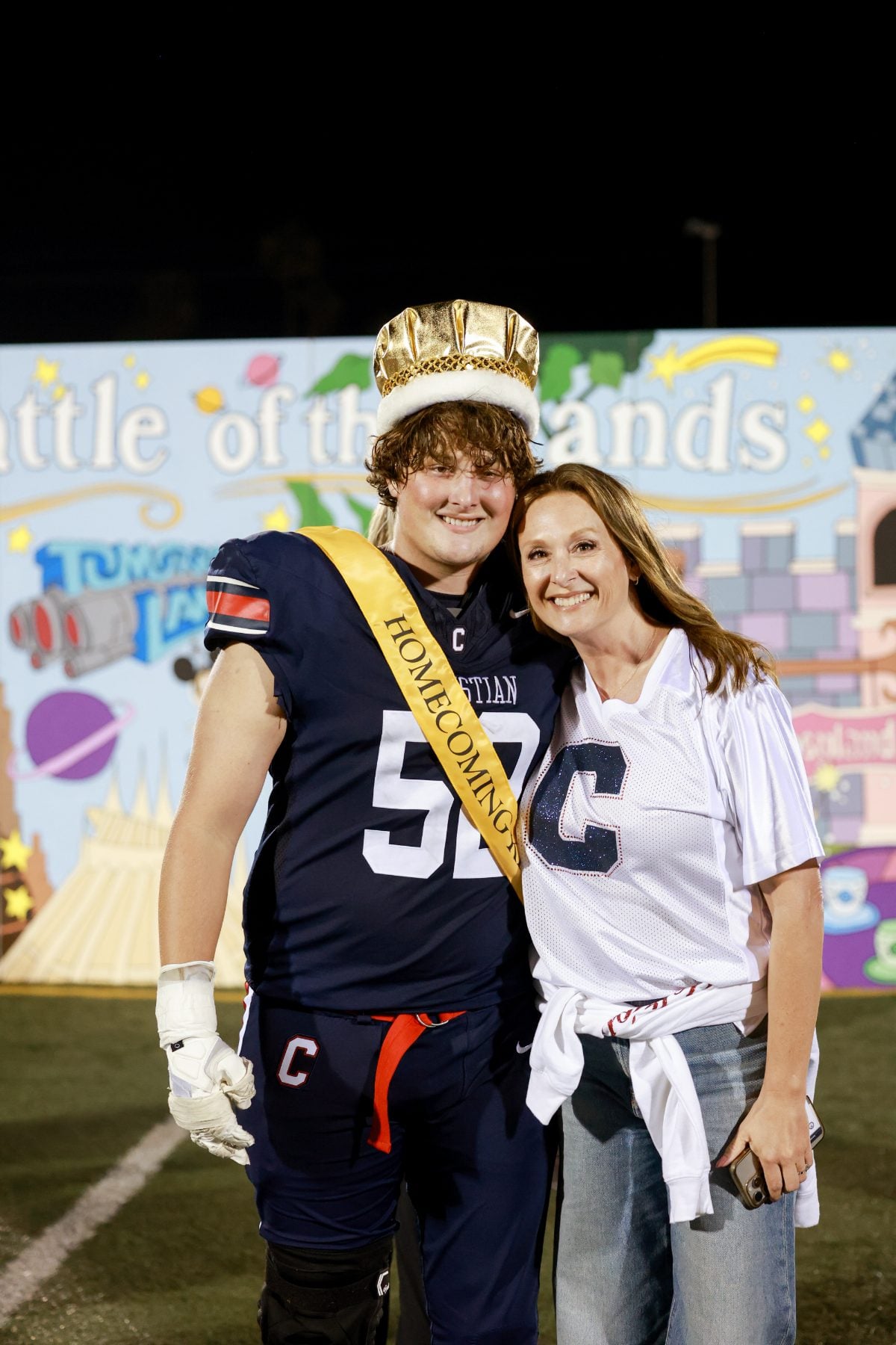 Football player wearing crown and sash poses with a woman after Homecoming win