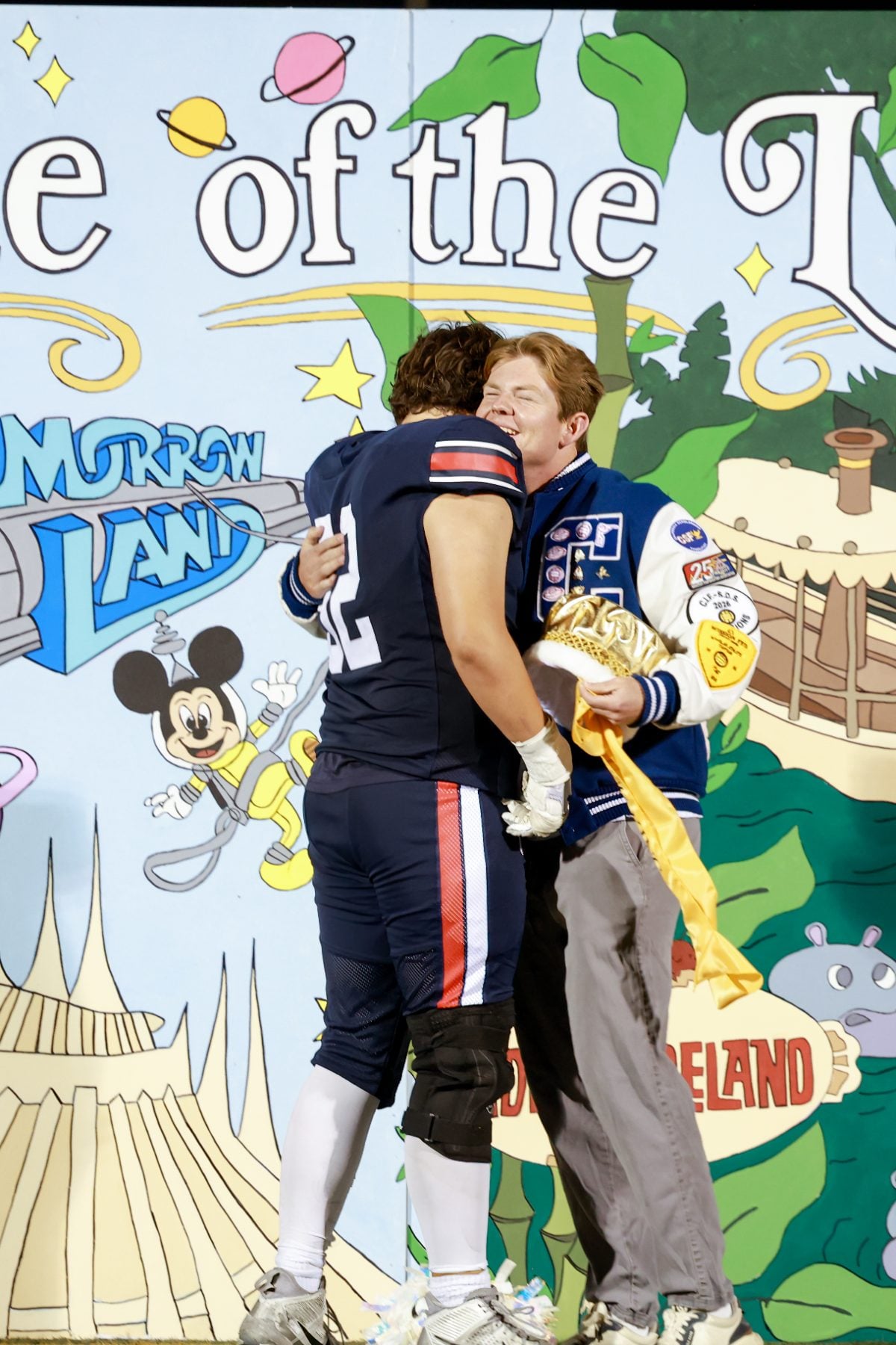 Football player embraces a student in front of Tomorrowland-themed homecoming backdrop