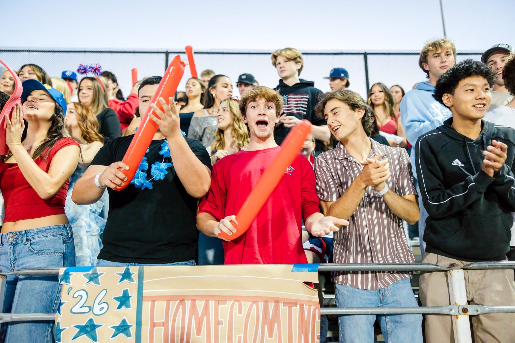 Students cheer with orange noisemakers beside a Homecoming sign