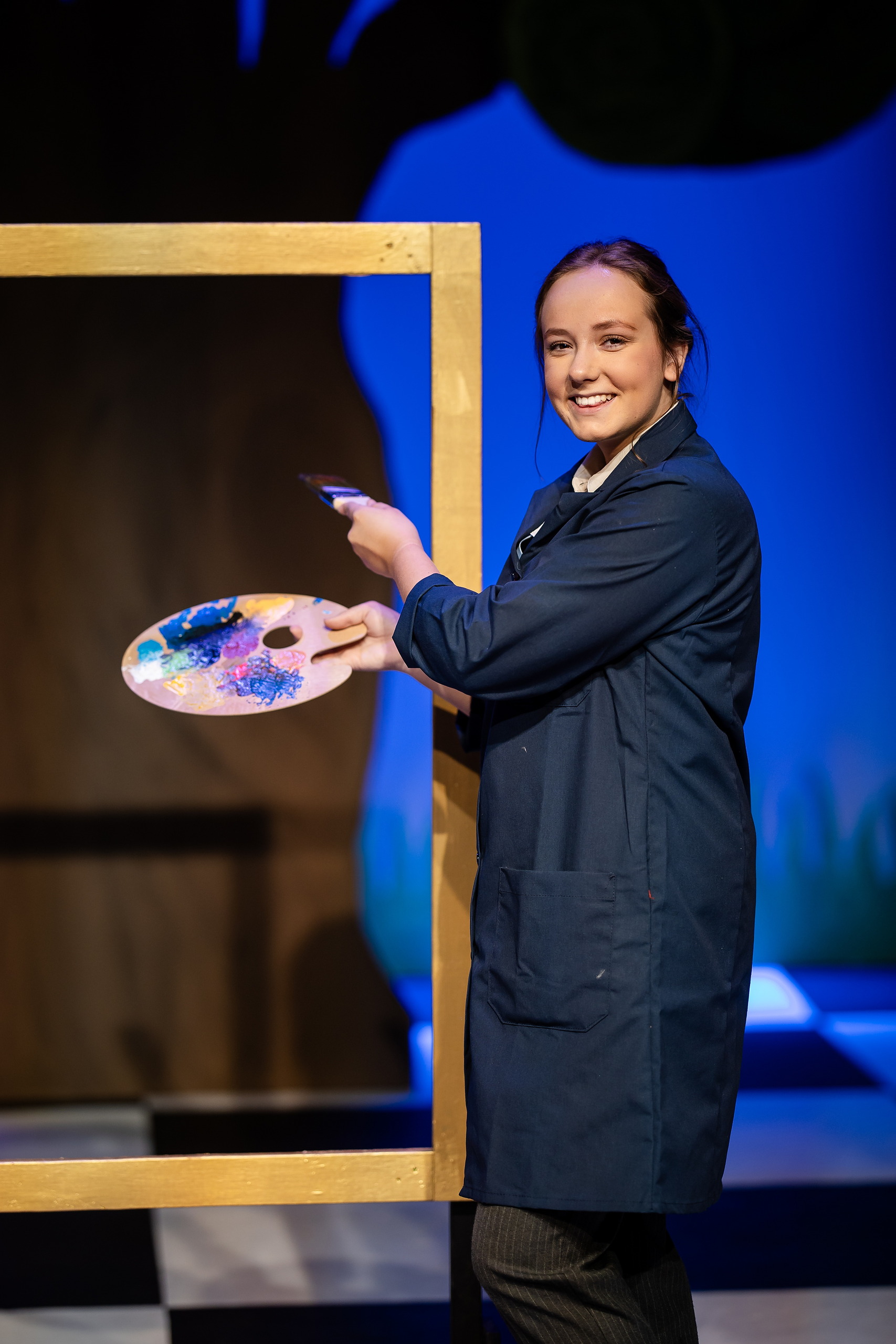 Curiouser and Curiouser! A Whimsical Journey with the Patriot Players — 01 Student in artist costume holds colorful painter's palette on stage