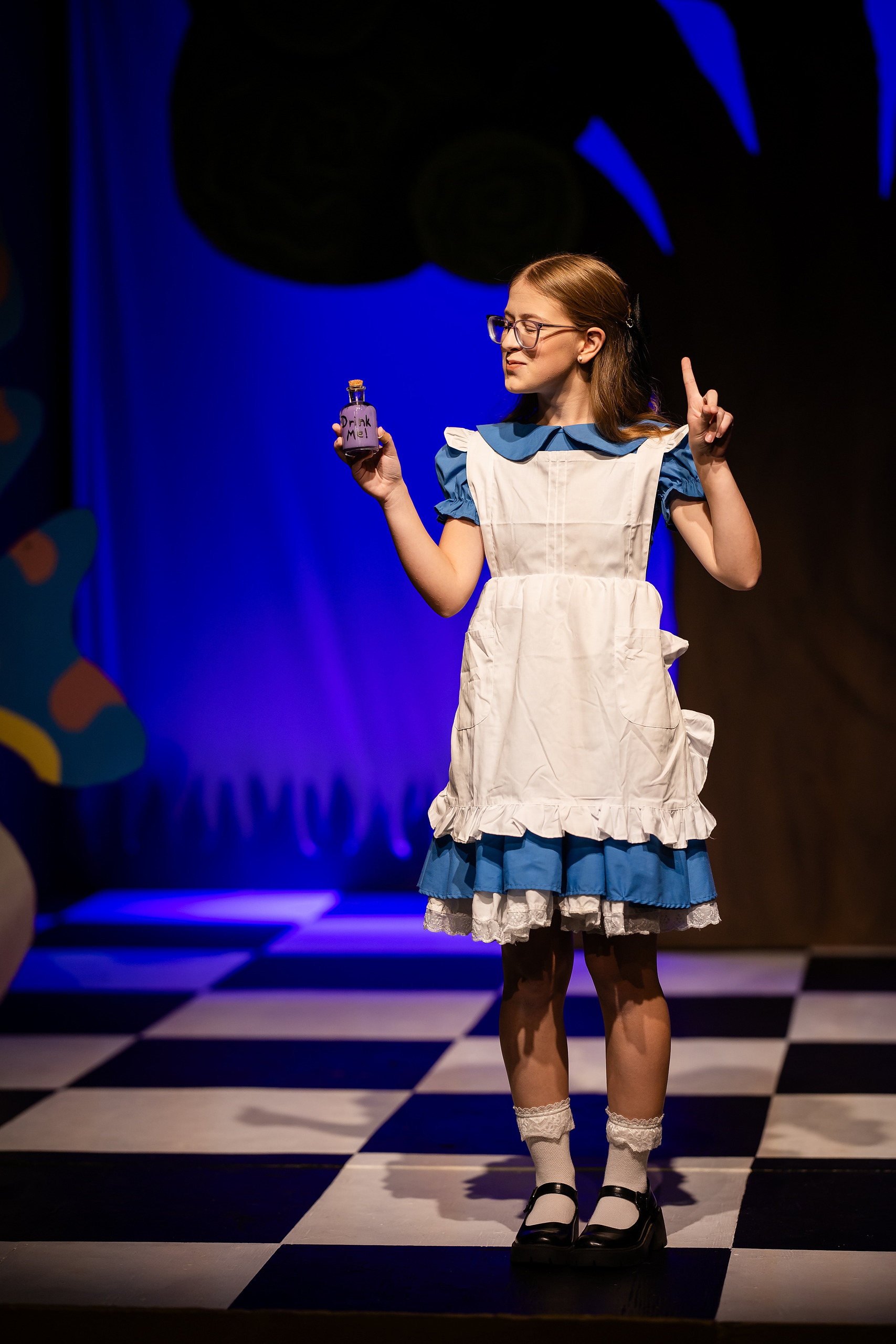 Curiouser and Curiouser! A Whimsical Journey with the Patriot Players — 03 Alice character holds small decorative potion bottle during scene