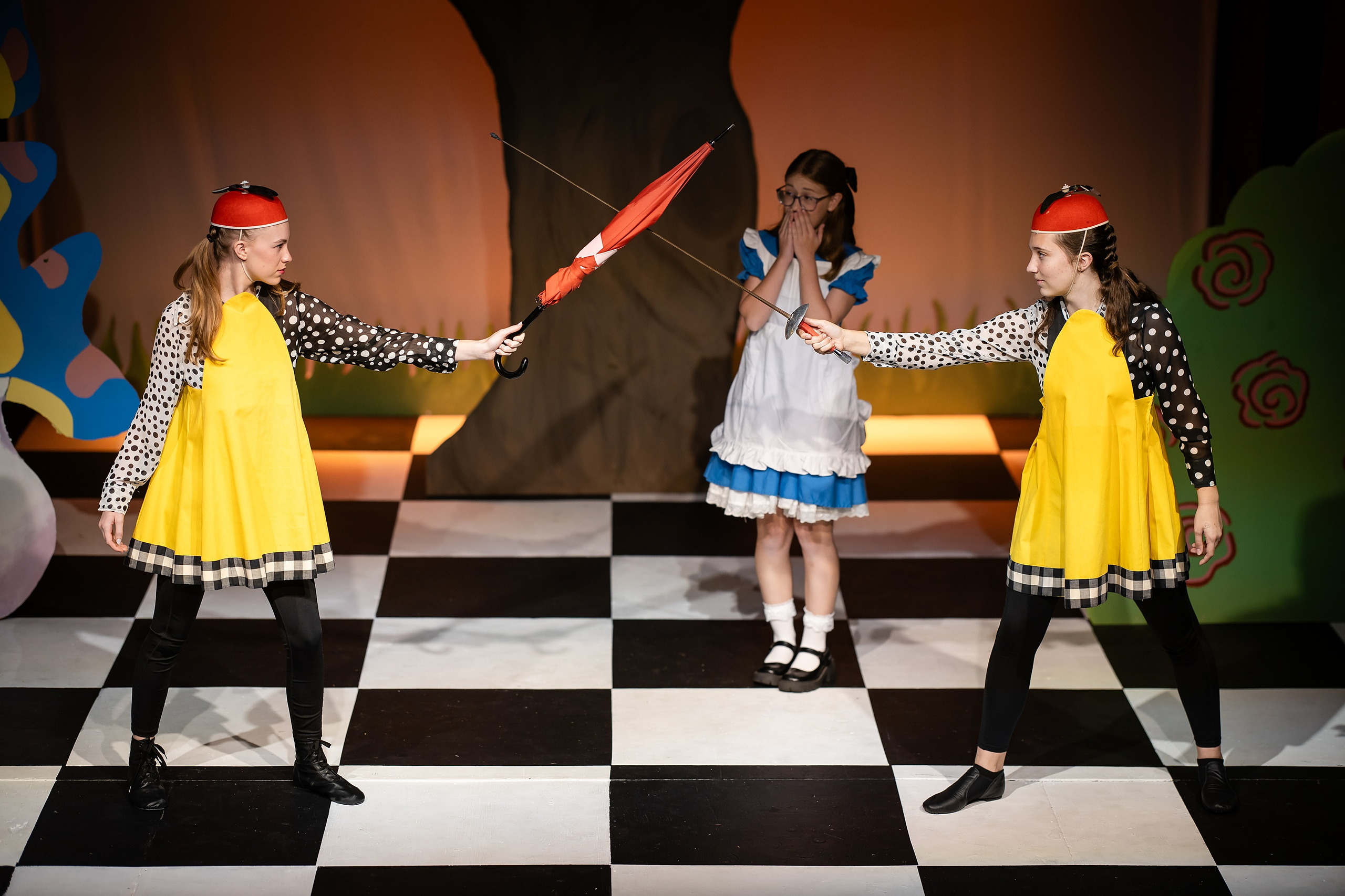 Curiouser and Curiouser! A Whimsical Journey with the Patriot Players — 04 Three students in yellow Tweedle costumes with polka dots hold props