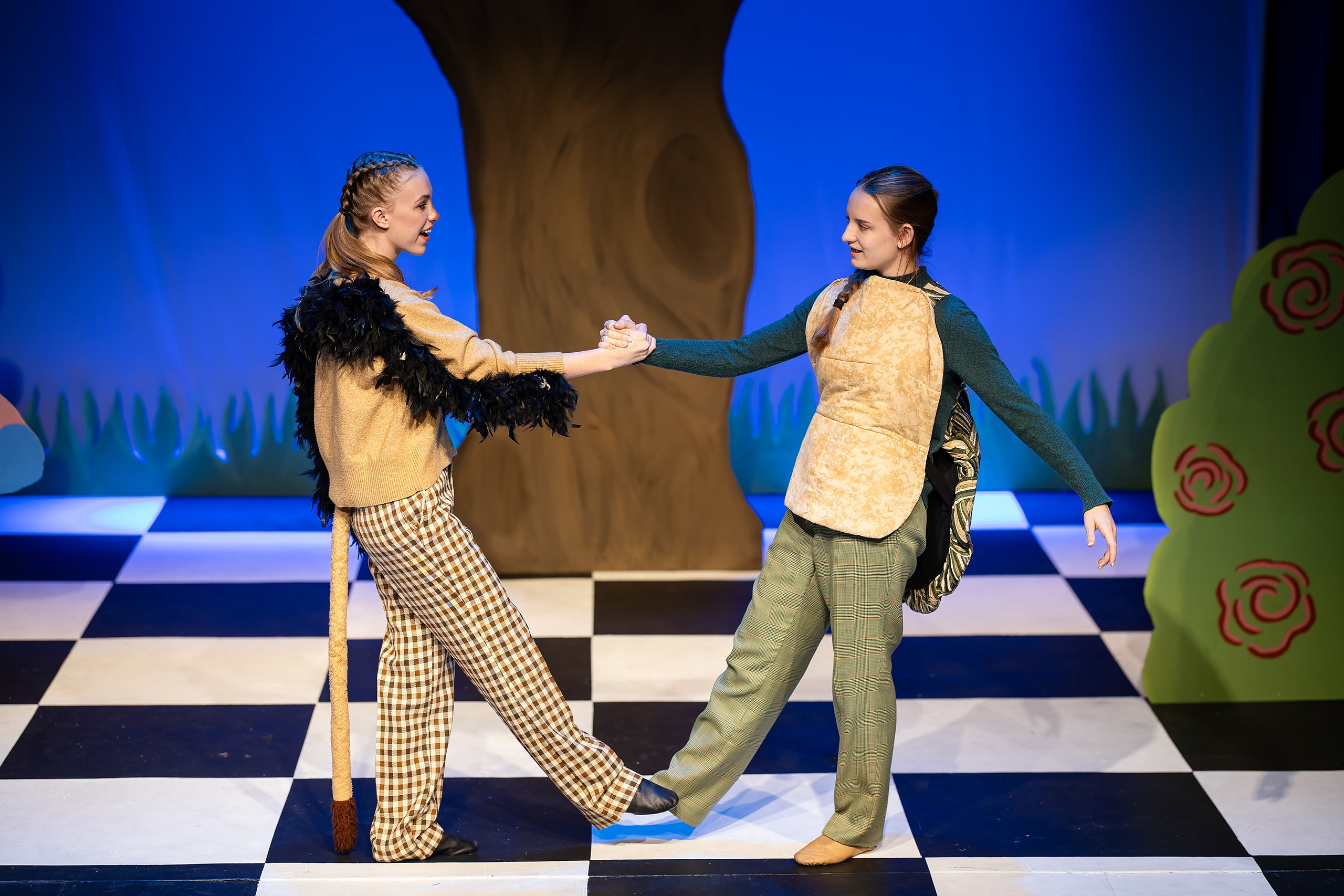 Curiouser and Curiouser! A Whimsical Journey with the Patriot Players — 07 Two Tweedle characters in patterned costumes hold hands on stage