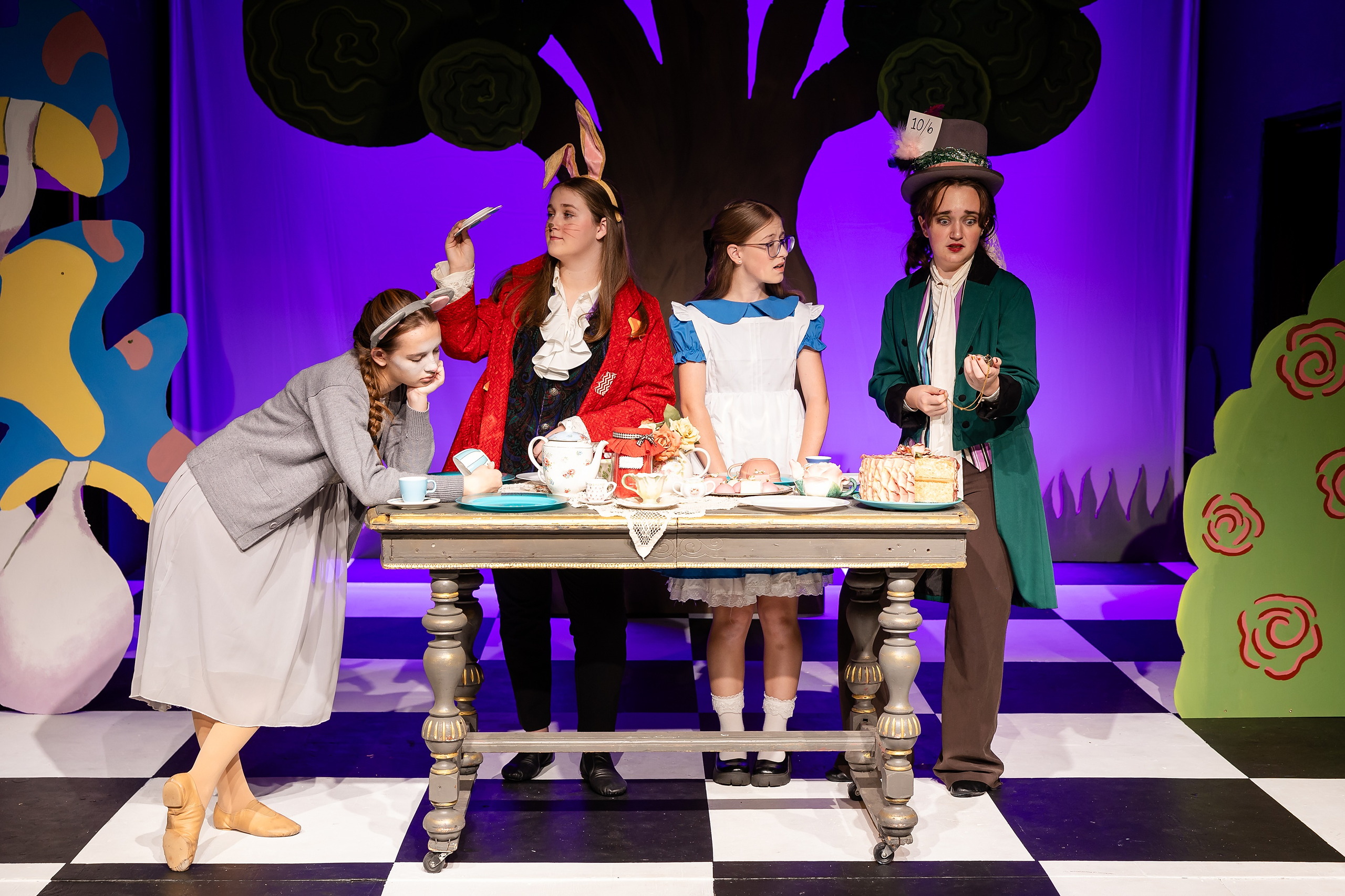 Curiouser and Curiouser! A Whimsical Journey with the Patriot Players — 12 Mad Hatter in green coat and tall hat serves tea during scene
