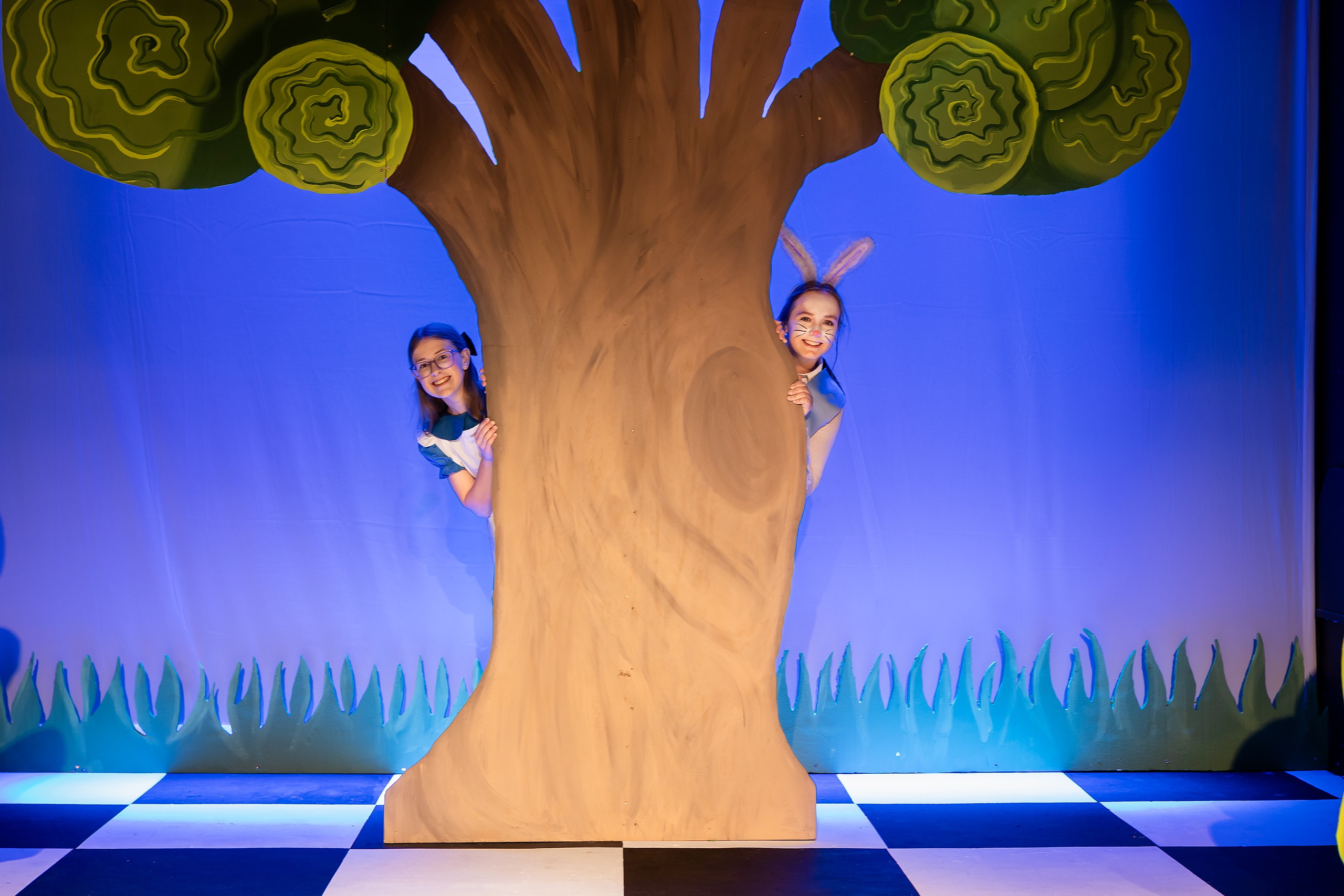 Curiouser and Curiouser! A Whimsical Journey with the Patriot Players — 16 Two Tweedle students in yellow costumes interact with Alice on stage
