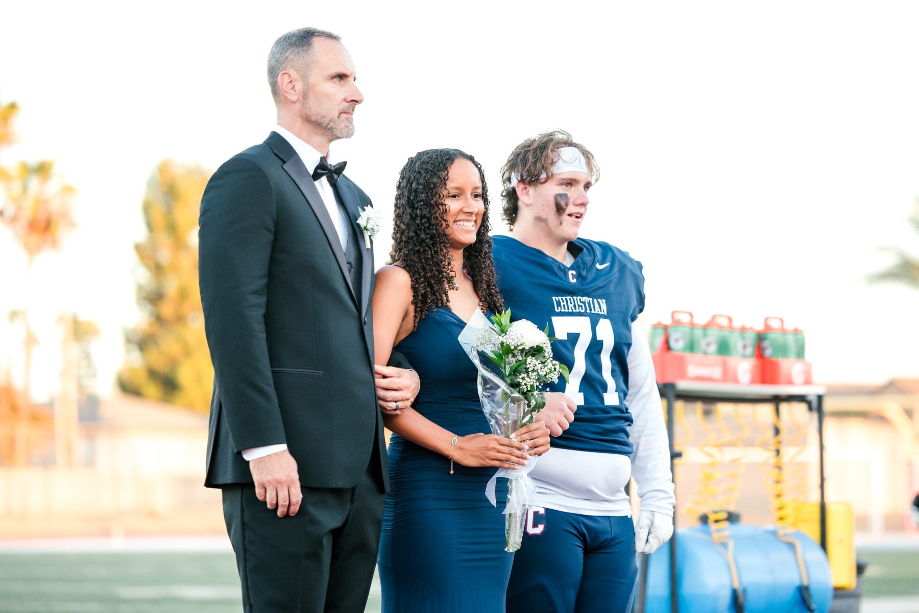 Homecoming court walks together on the field with a bouquet