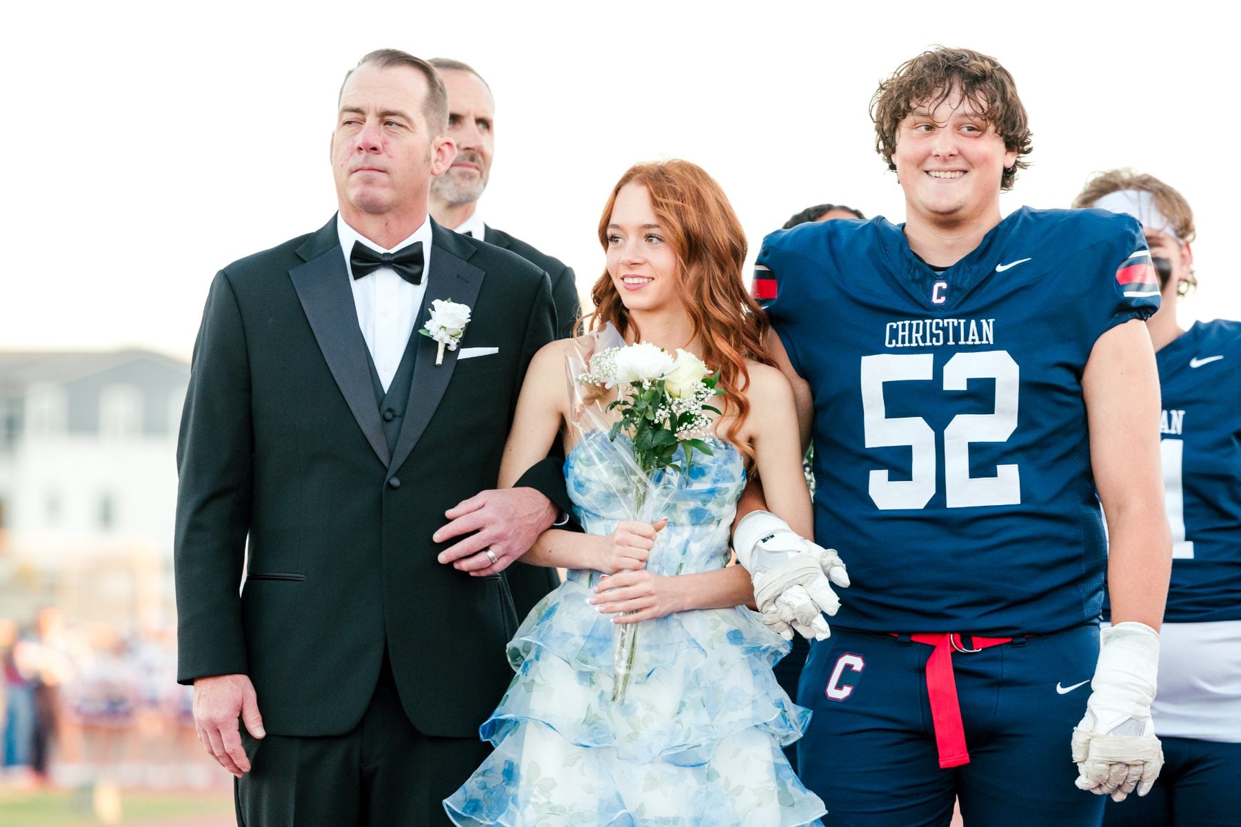 Homecoming court student walks with her father and a Patriots football escort
