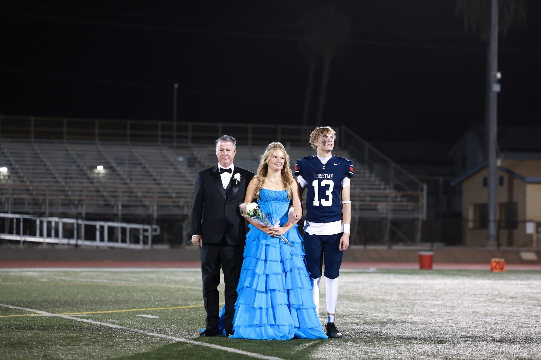 Homecoming court stands on the football field under stadium lights