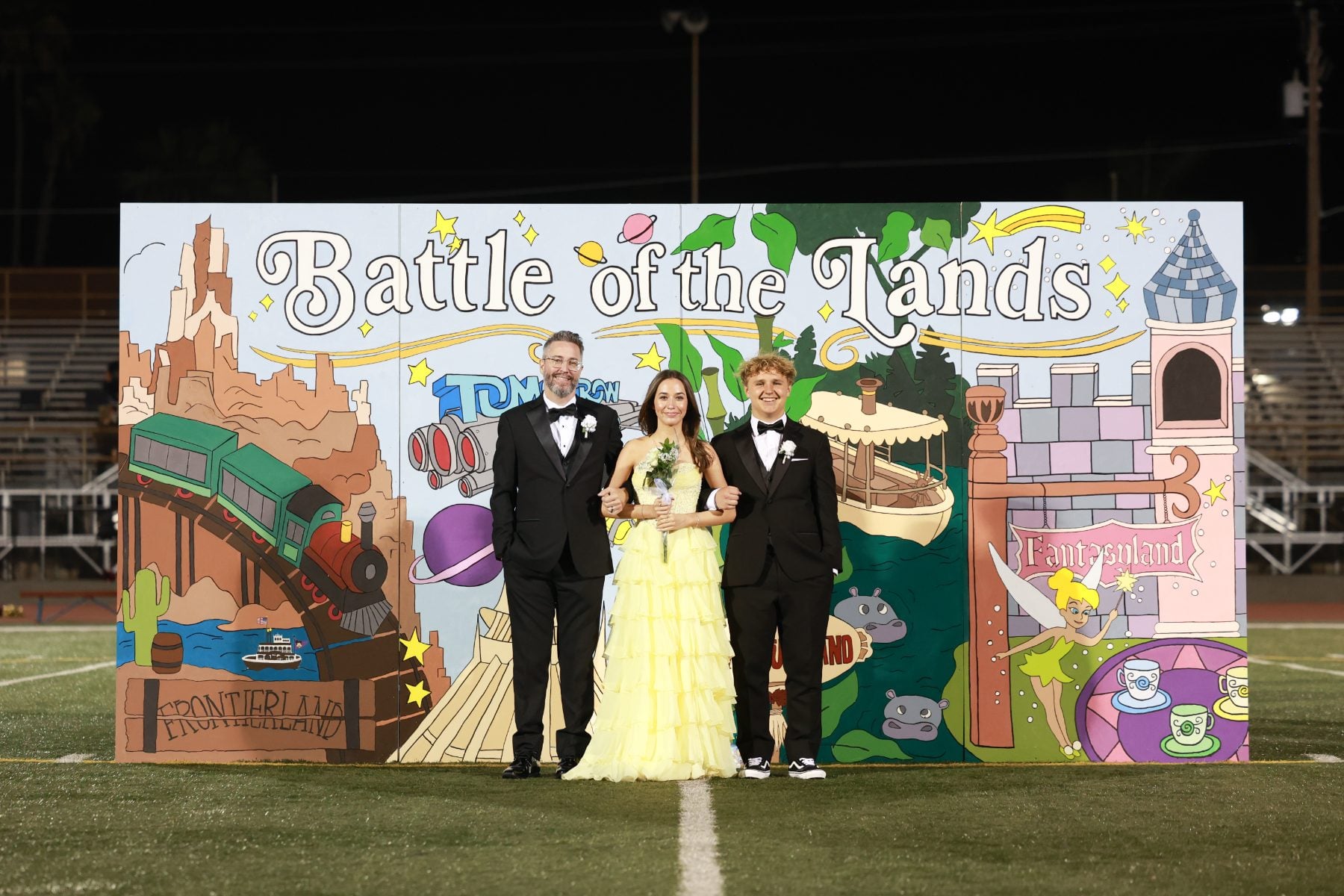 Homecoming court trio poses in formal wear at Battle of the Lands backdrop