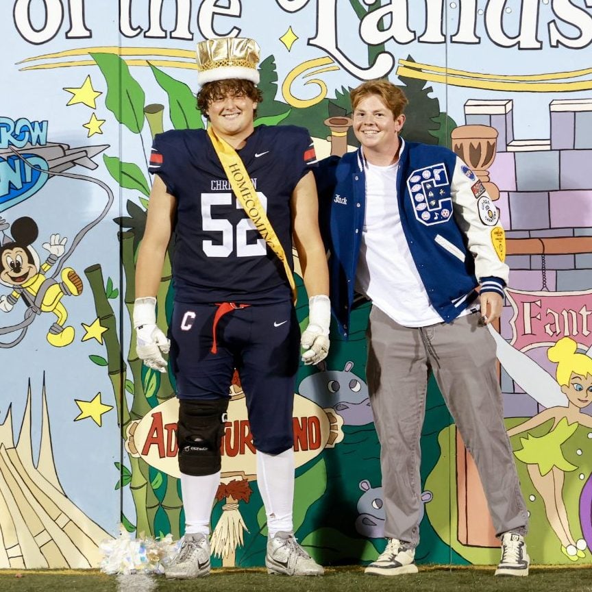 Crowned homecoming king stands with a student at Adventureland-themed backdrop