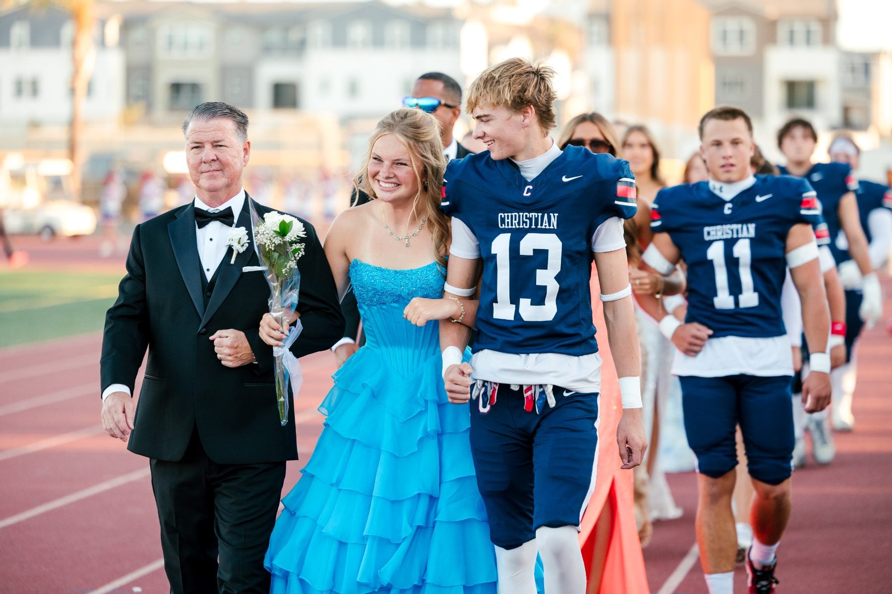 Homecoming queen candidate in teal gown walks arm-in-arm with her father
