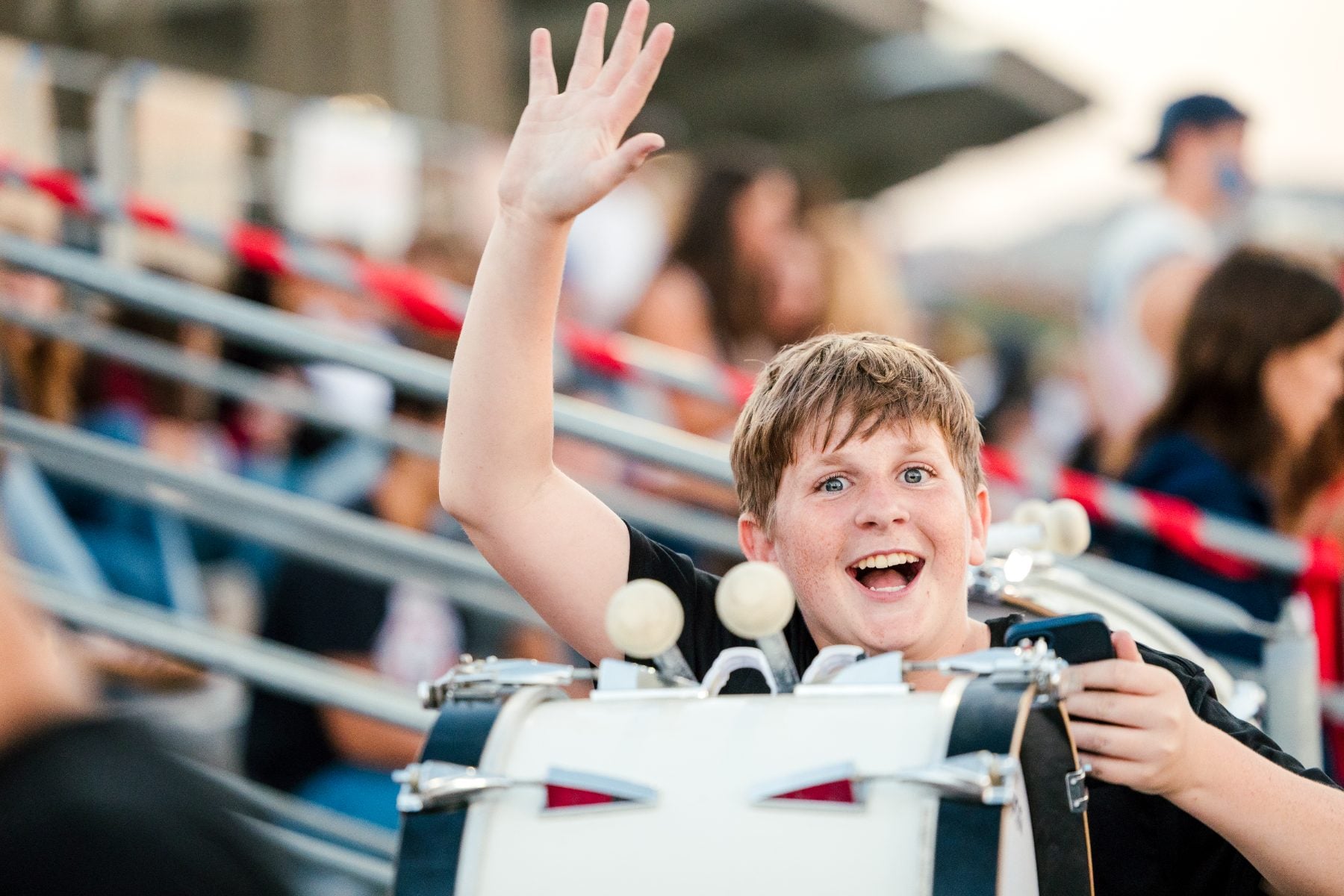 A drummer in the marching band waves and smiles during Homecoming night