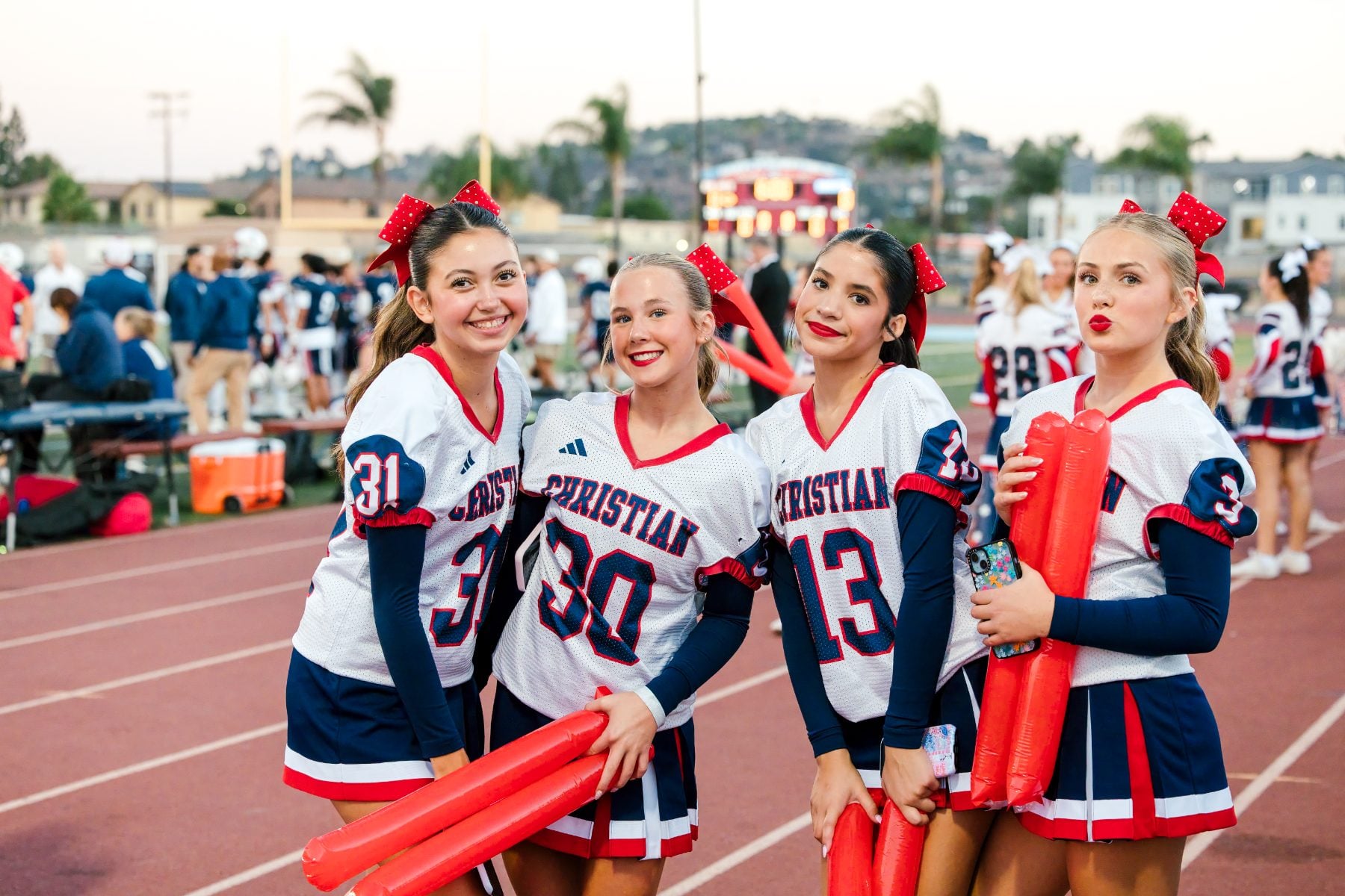 Four cheerleaders in Patriots uniforms pose with red pom sticks on the track