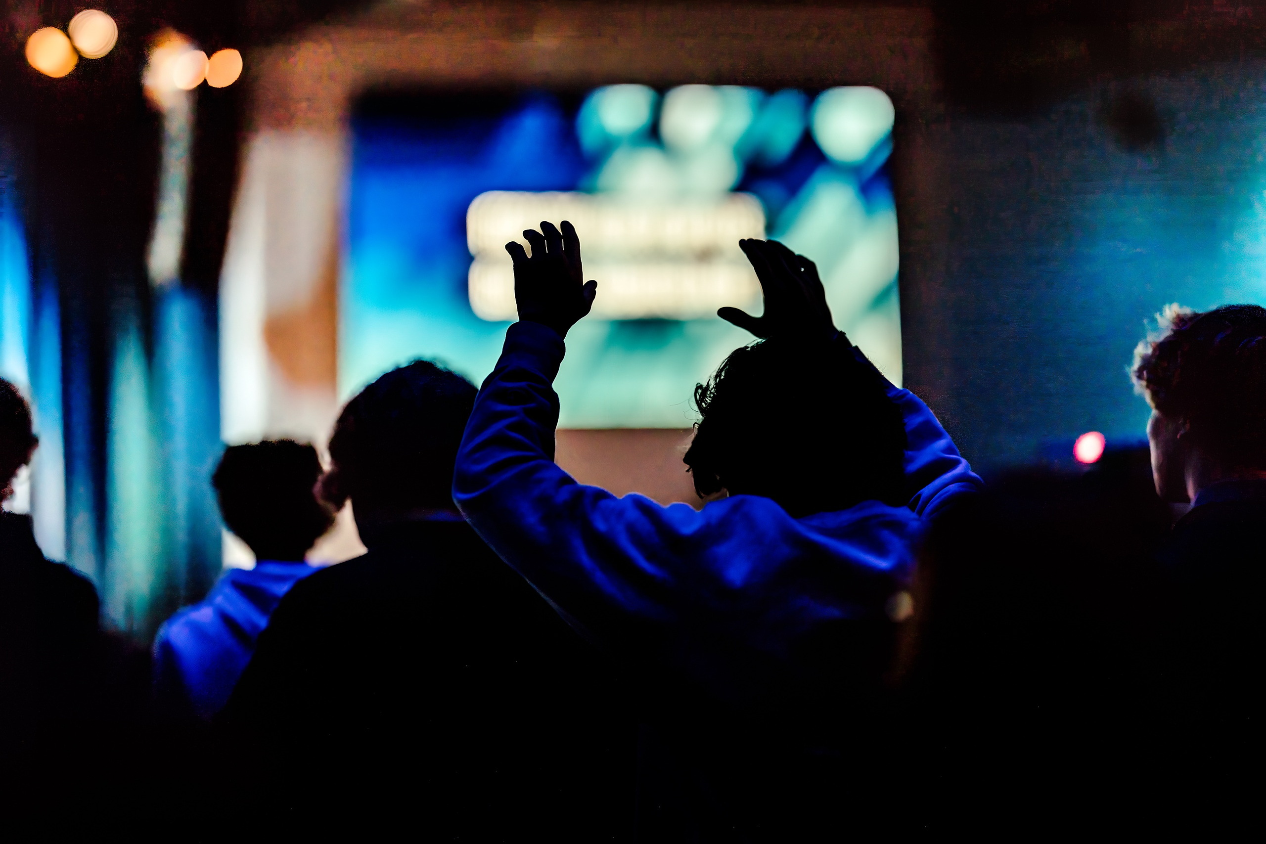 Spiritual Emphasis Week 2025 — 02 Students raise their hands during worship with blue stage lighting