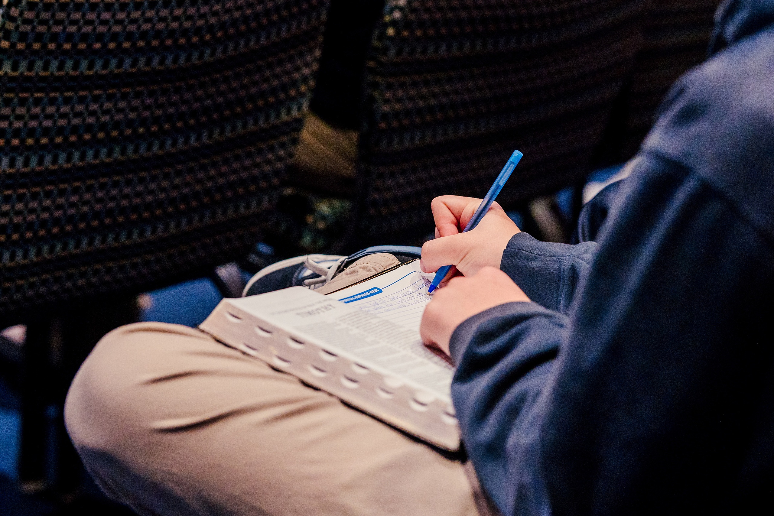 Spiritual Emphasis Week 2025 — 12 Student's hands write notes on paper during chapel teaching session