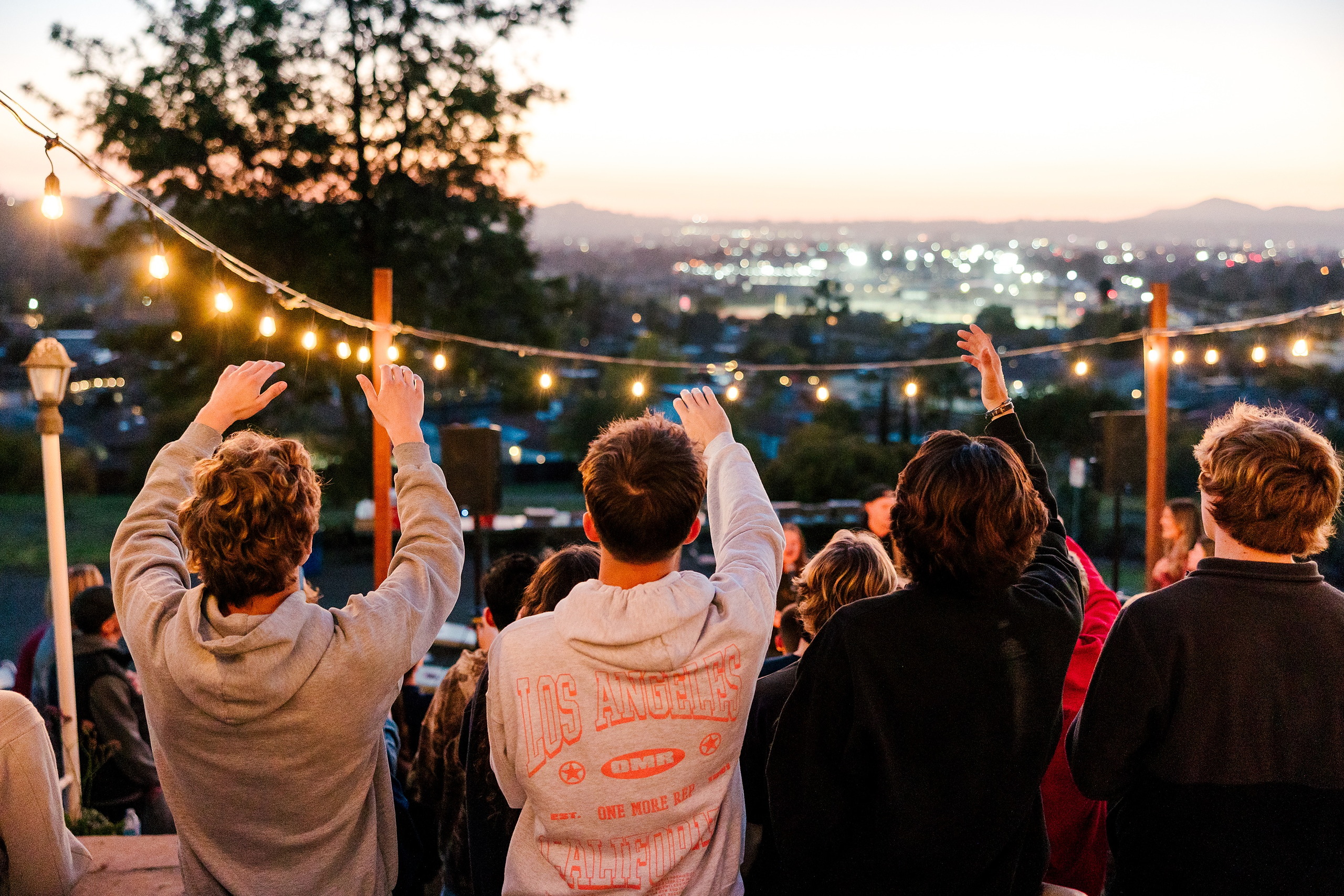 Spiritual Emphasis Week 2025 — 38 Teens with hands raised during evening worship near fire pit