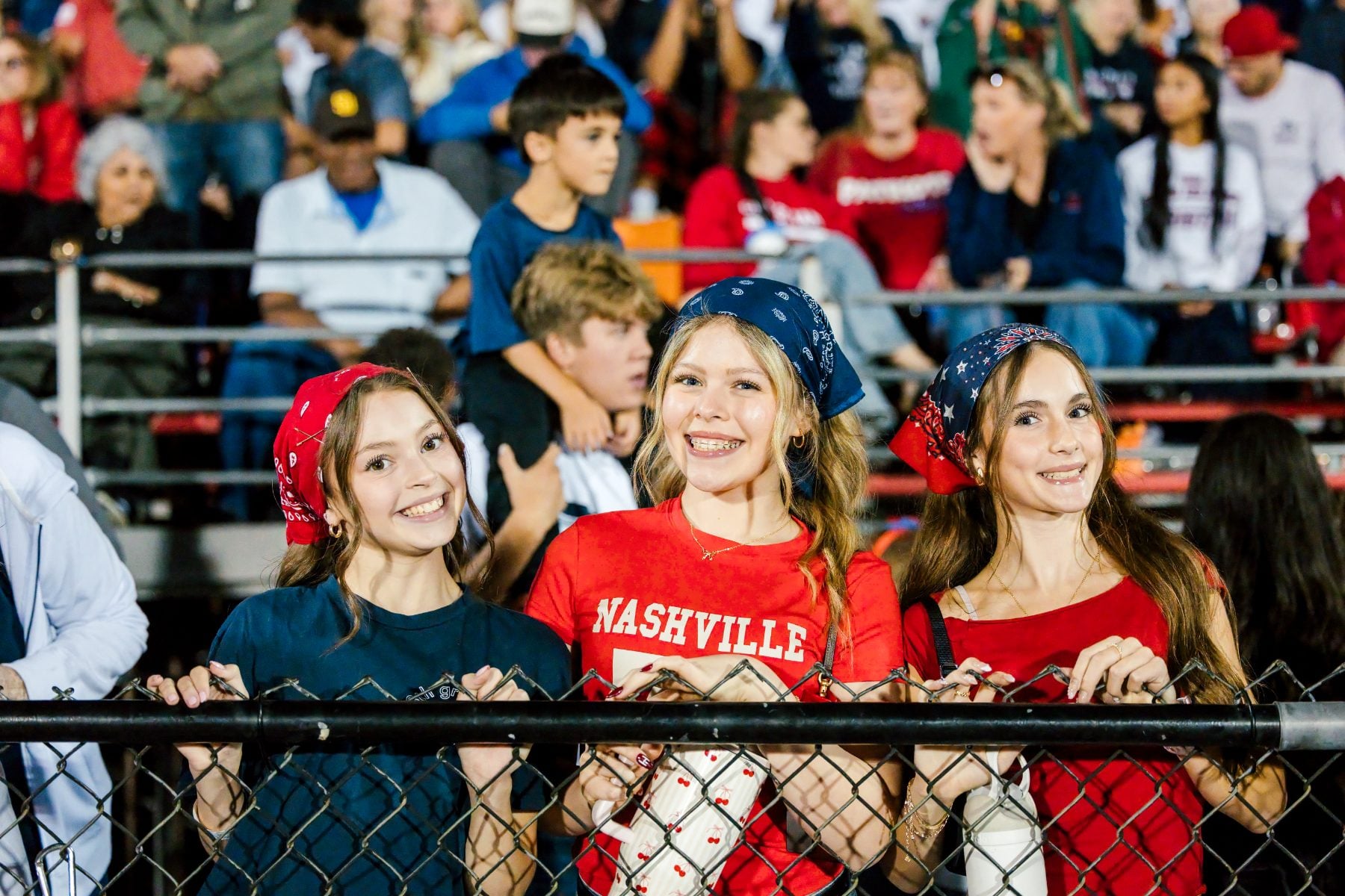 Three students in red bandanas smile together in the homecoming crowd