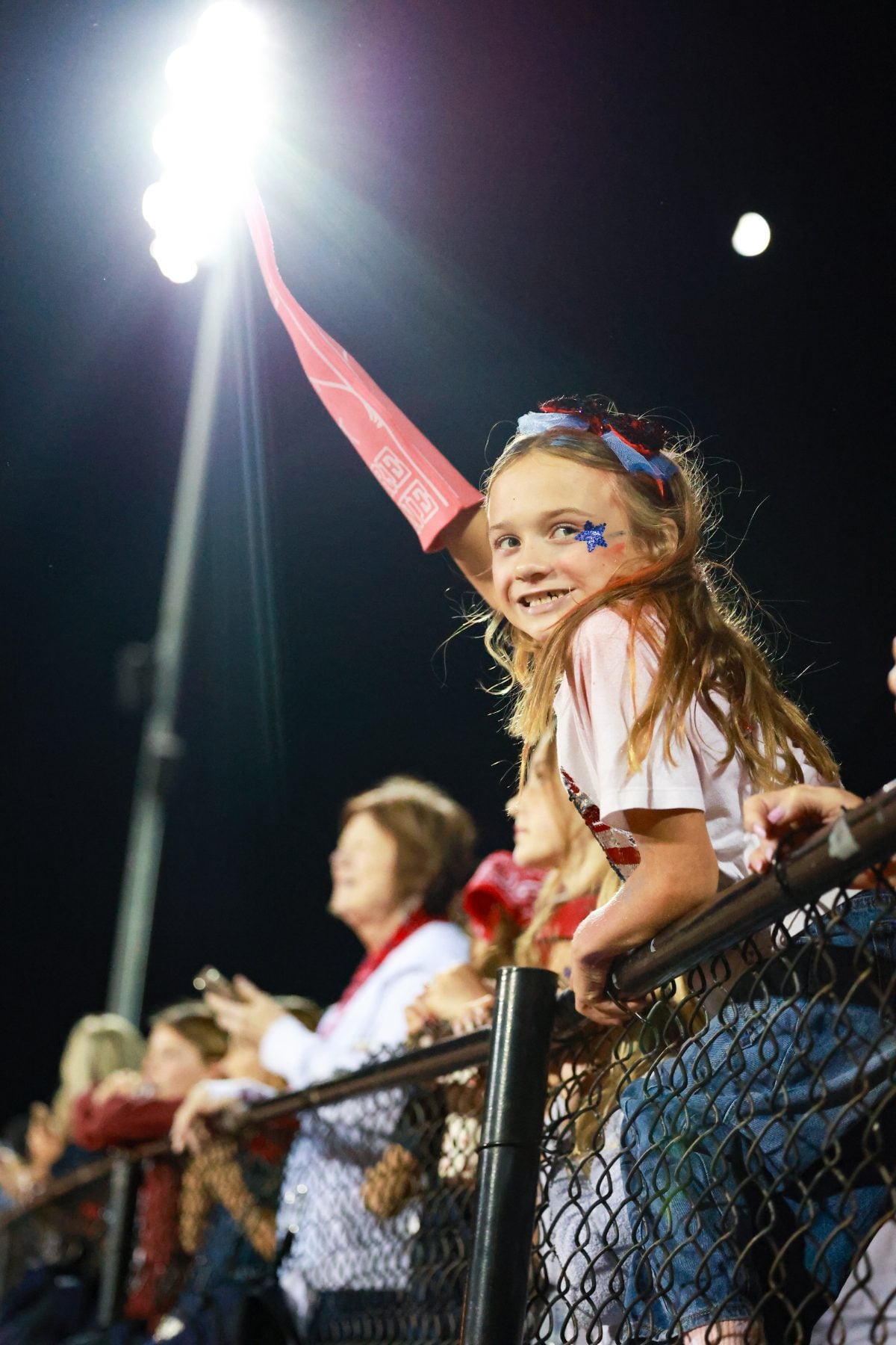 Young fan waves red pennant from bleachers during a nighttime football game