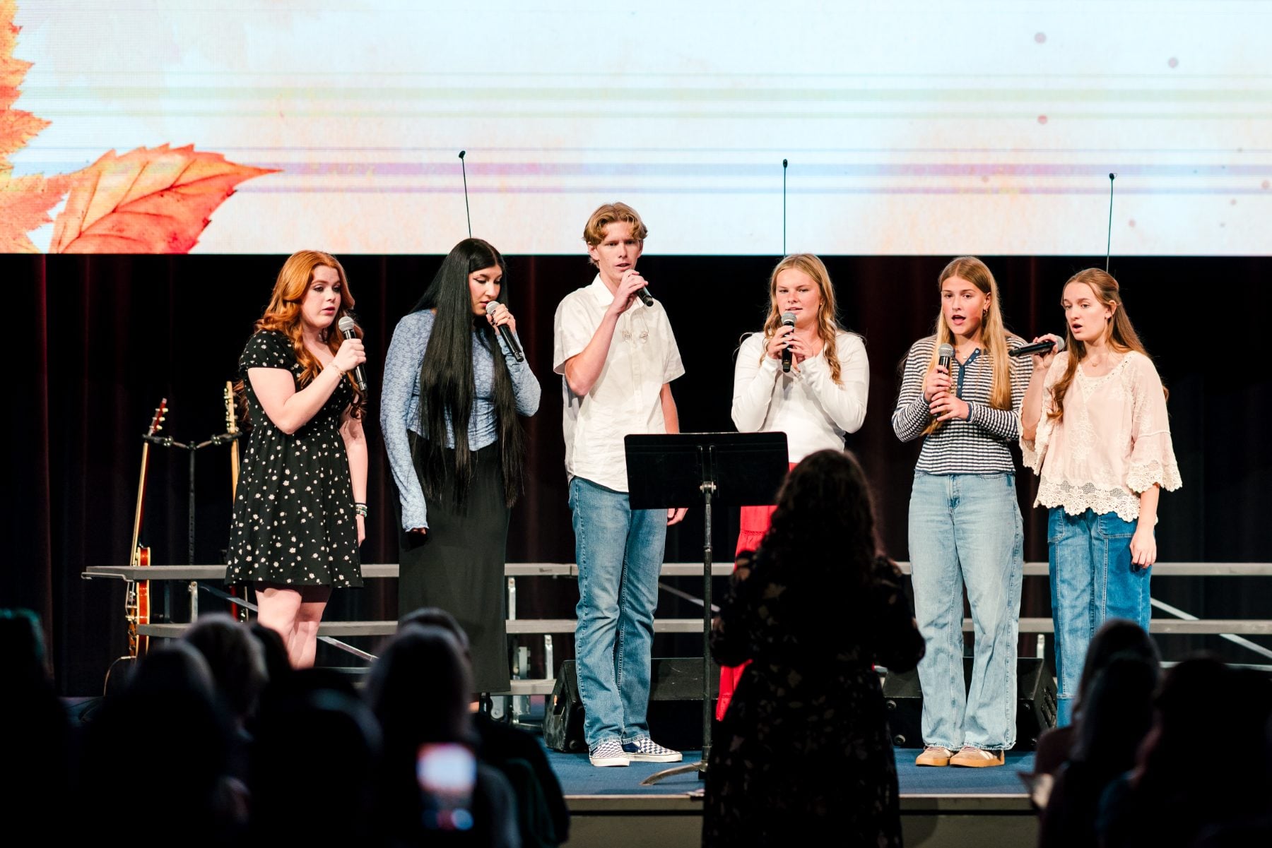 Six students harmonize together in a group performance on stage