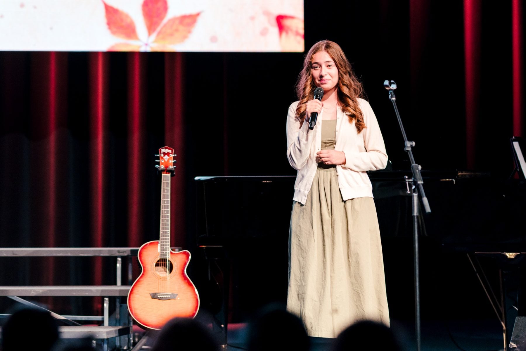 Student in cardigan holds sheet music while singing at Event Center stage