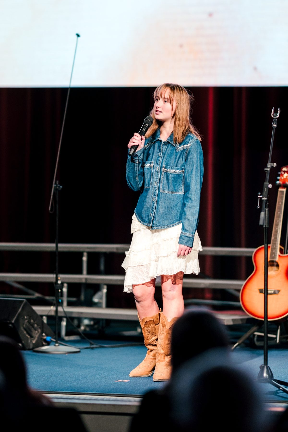Student in denim shirt and cowboy boots sings solo on stage