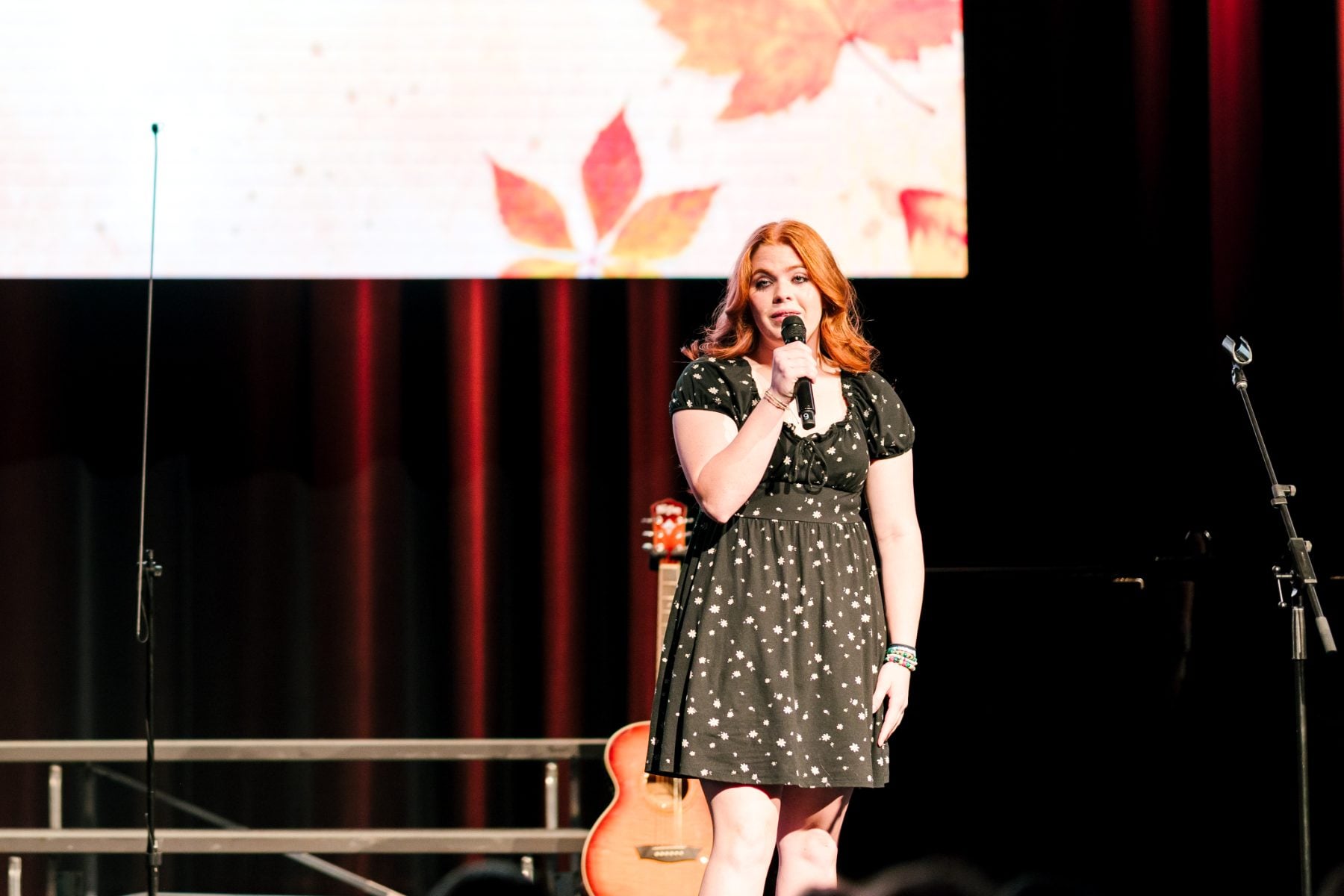 Student in floral dress sings with autumn leaf backdrop at the concert