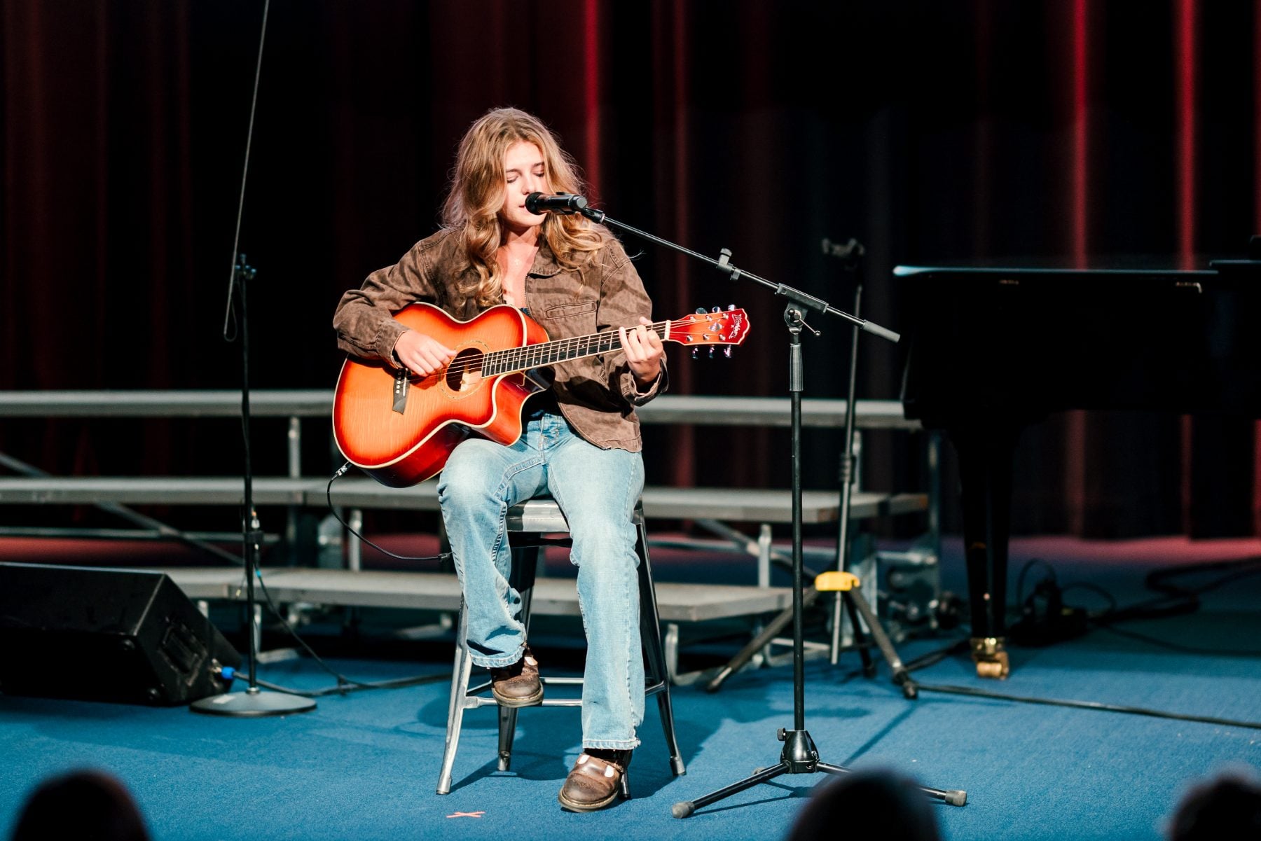 A student plays acoustic guitar while singing seated on a stool