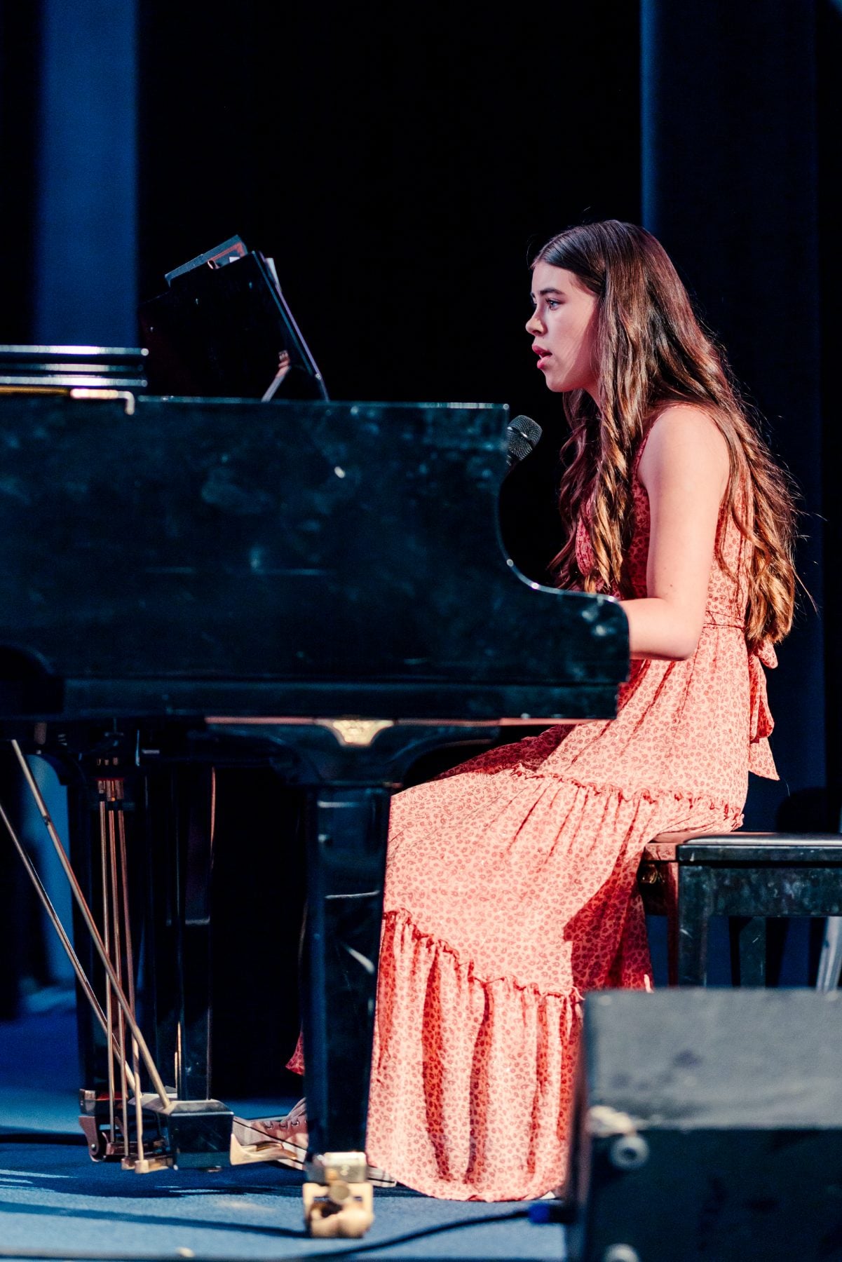 A student plays grand piano while singing at the Event Center