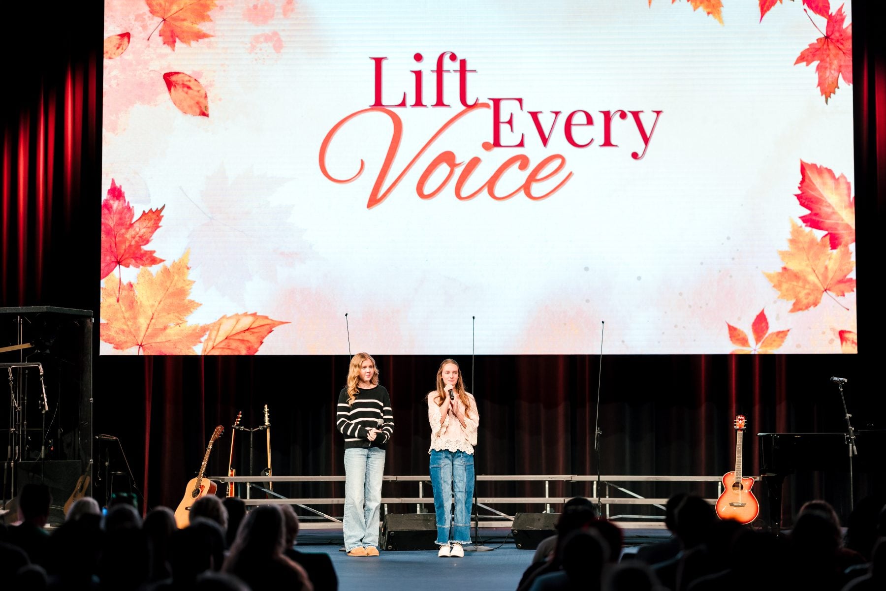 Two students stand together on stage under the Lift Every Voice title slide