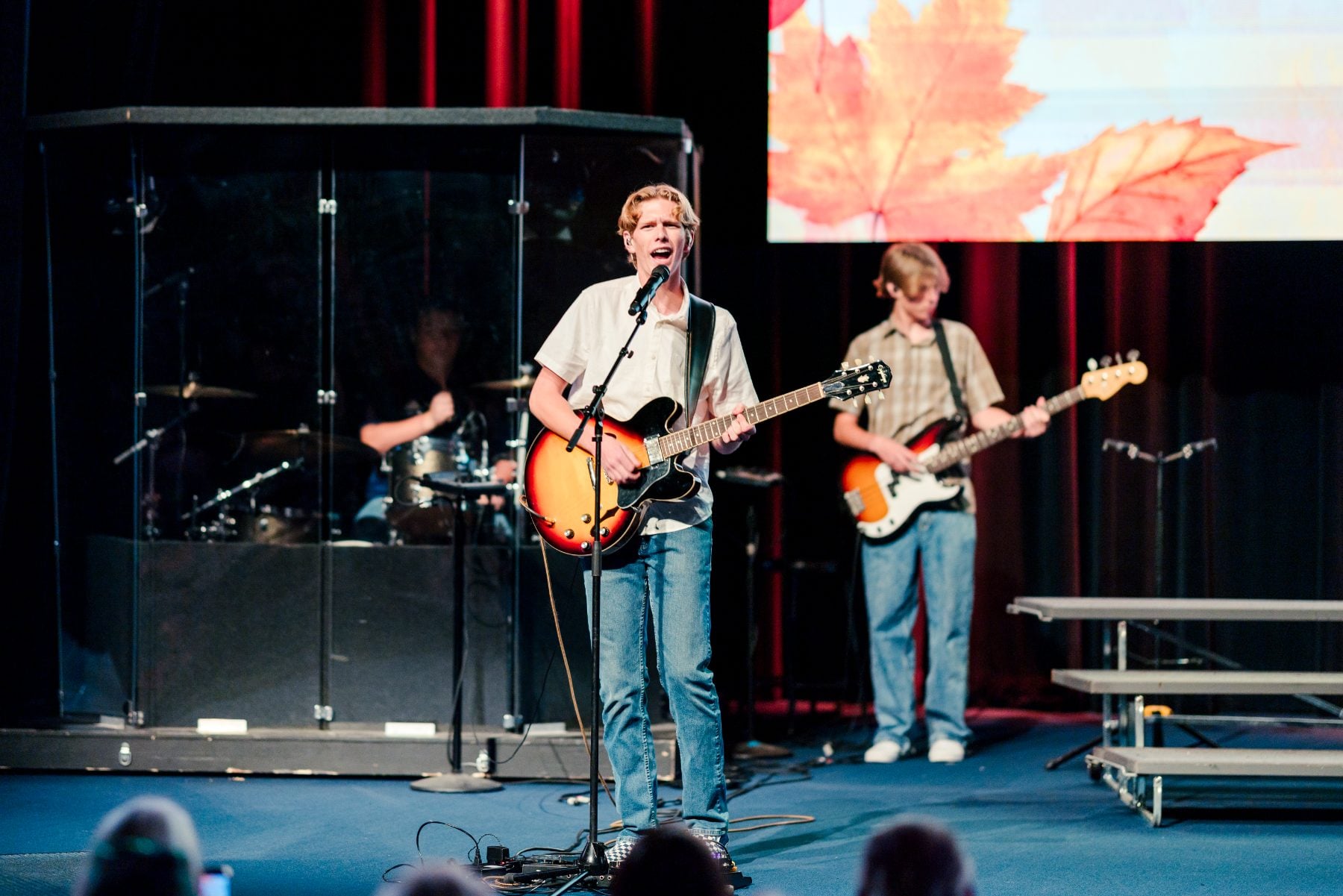 Students play guitar and drums during a band performance on stage.