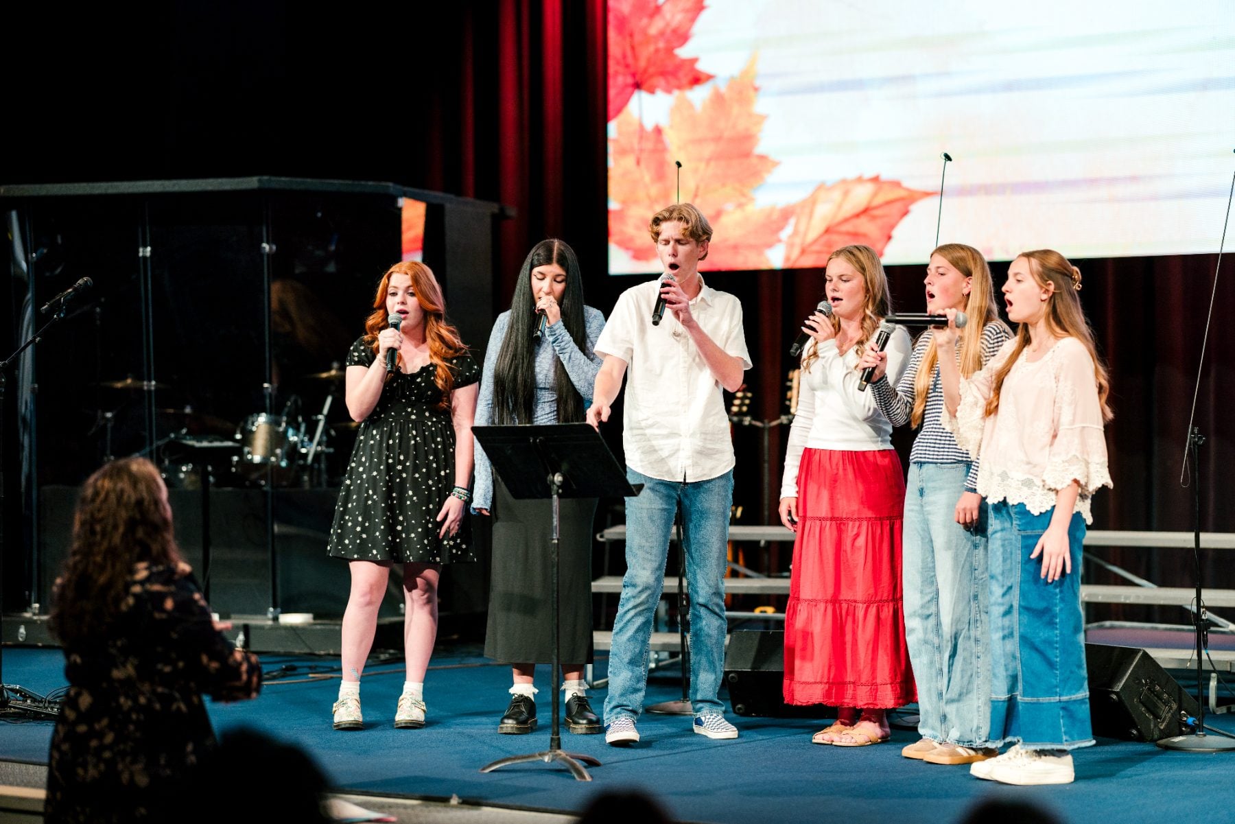 A small group of students sing together with microphones on stage.